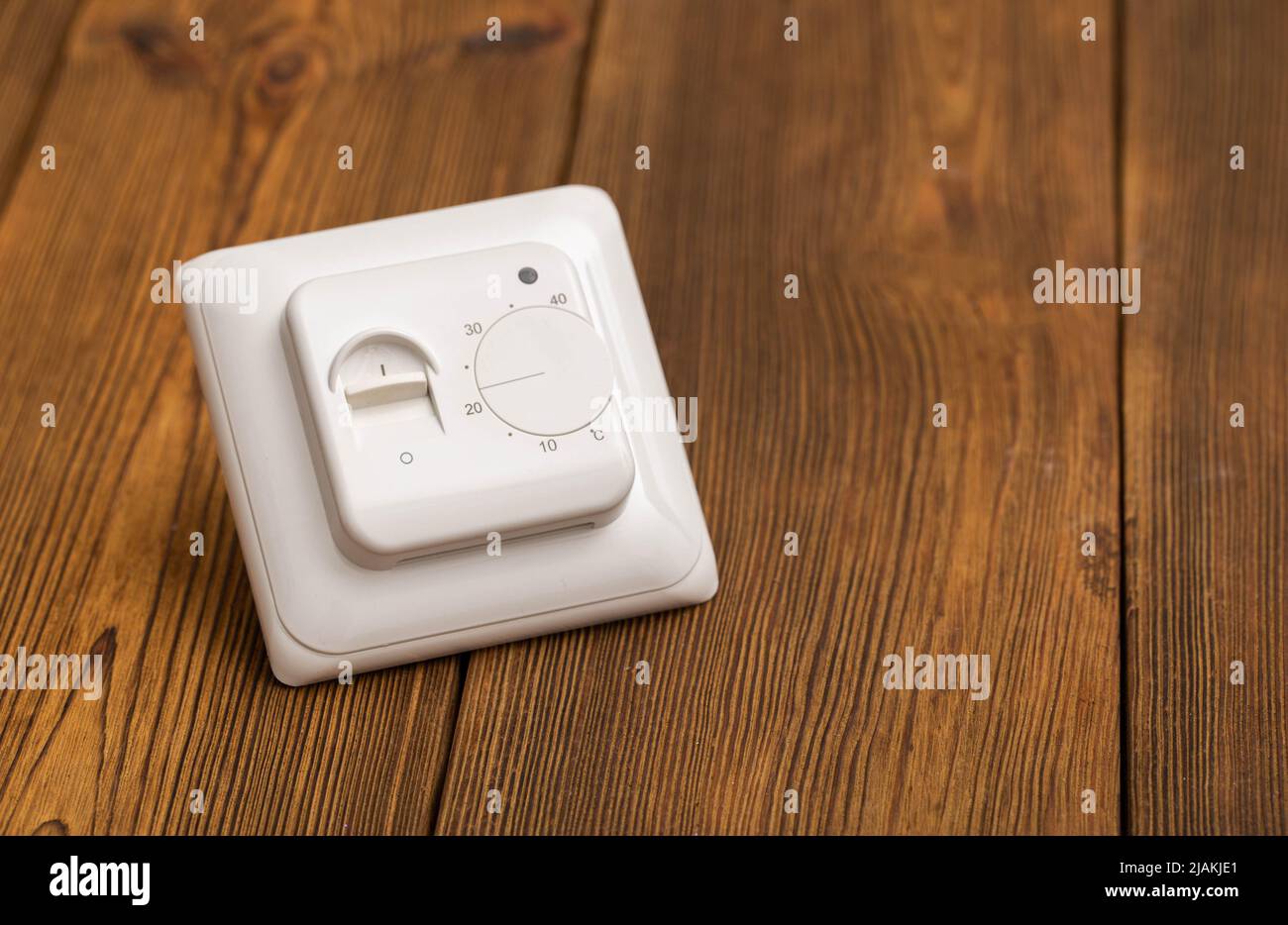 Electric thermostat for underfloor heating on a wooden background, close-up. Stock Photo