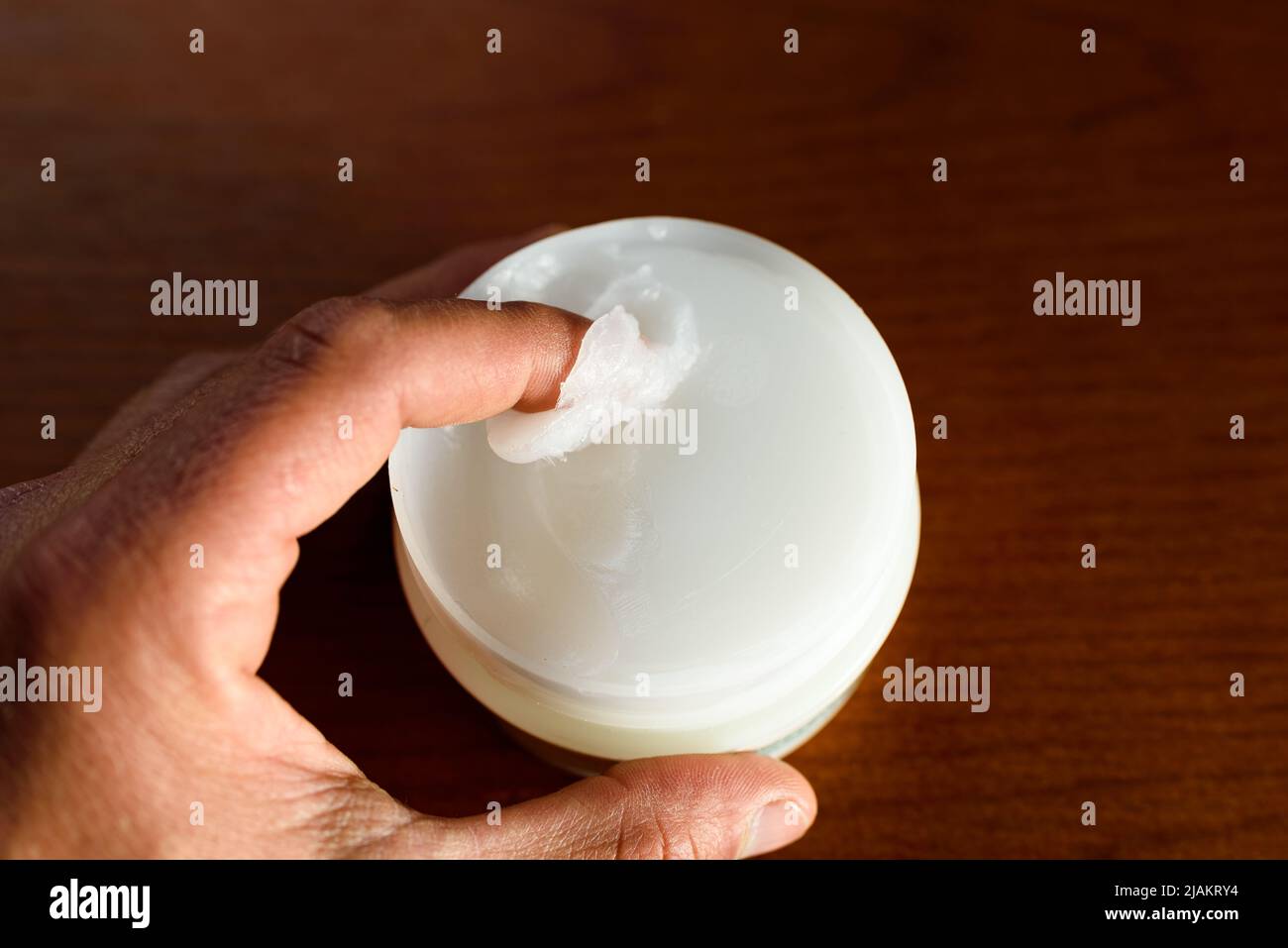 A man picks up white Vaseline to moisturize his skin, dark background. Stock Photo