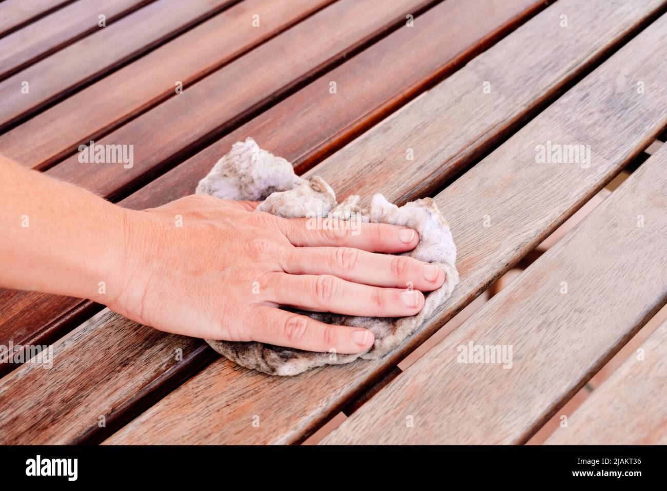Woman's hand with a dirty rag wipes a table from wooden boards. Stock Photo