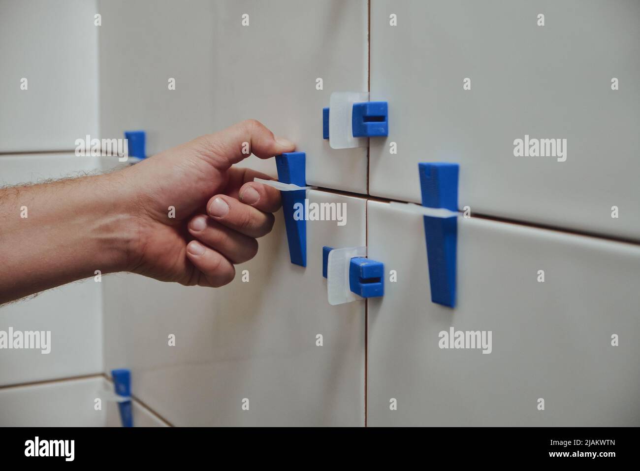 Tiler using tile leveling system when laying ceramic tiles on bathroom