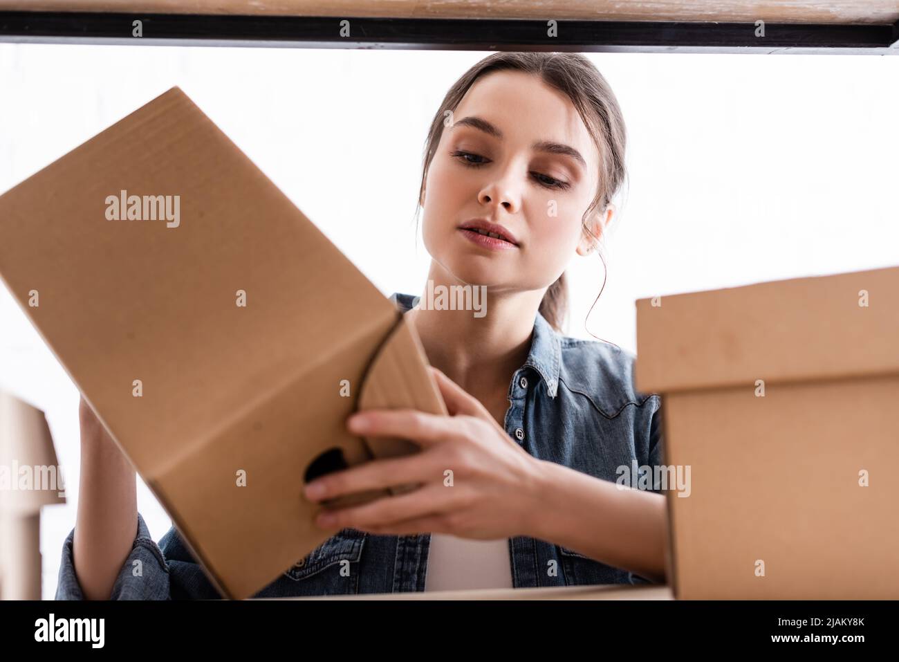 Young seller holding carton box near rack in online web store Stock Photo