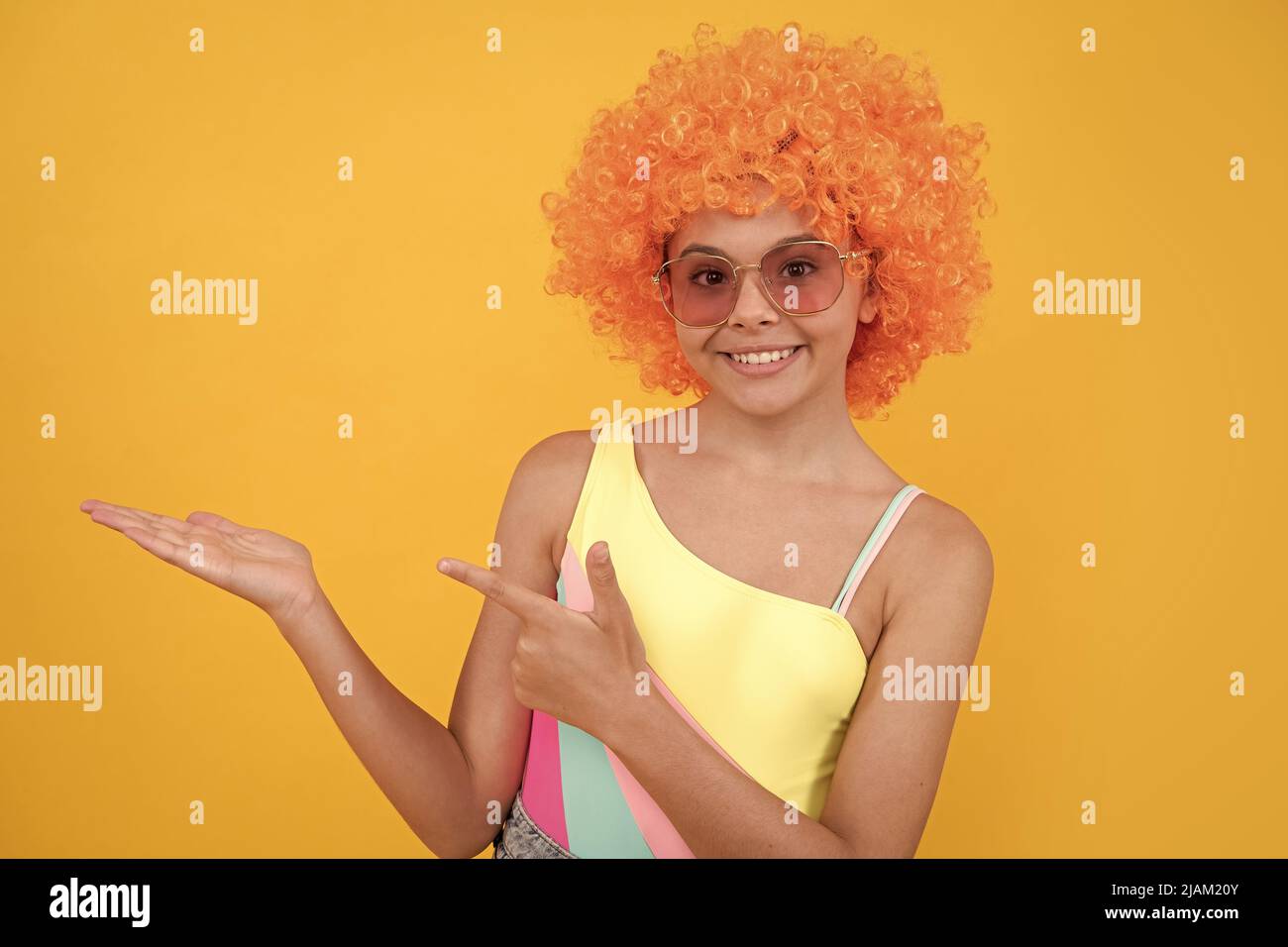 happy kid in sunglasses pointing finger on yellow background copy space