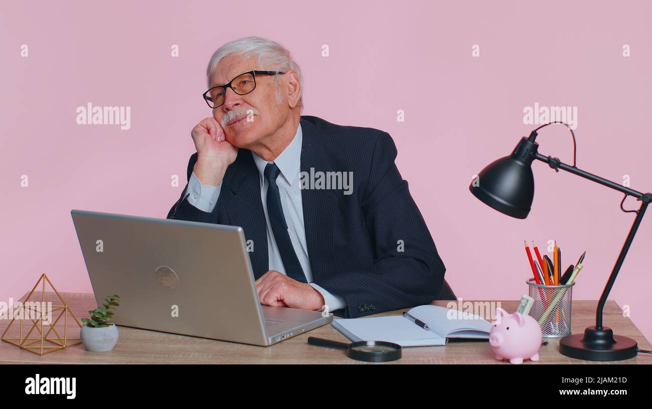 Senior businessman in thought and conjectures looking to side, dreaming, imagining something pleasant, fantasizing about weekends holidays. Elderly man isolated on pink studio background at office Stock Photo