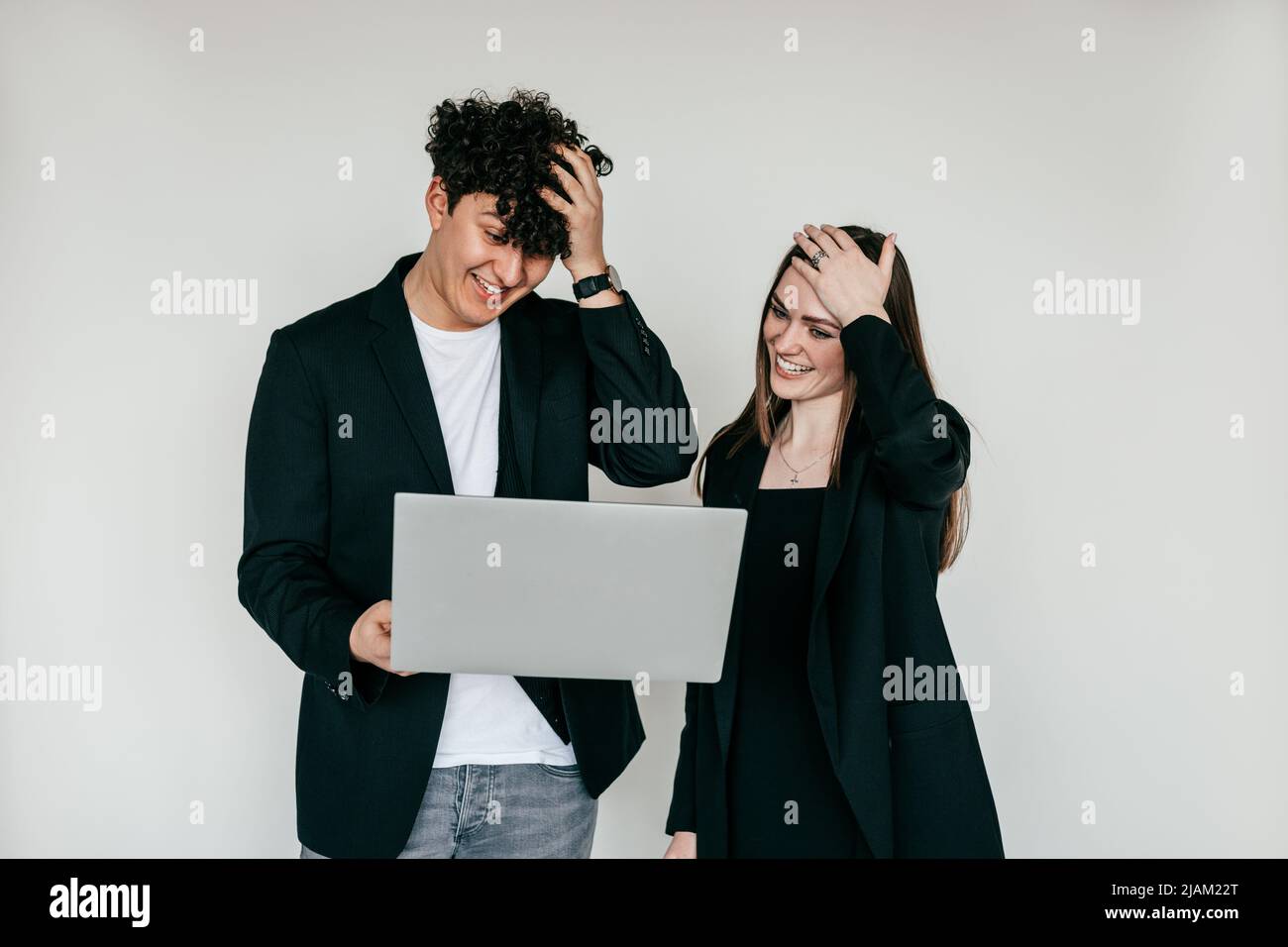 Two puzzled, surprised and shocked woman and man standing with laptop, looking at screen. Troubles in work, unbelievable Stock Photo