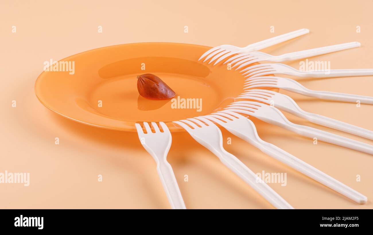 Plate with a small piece of sausage and a lot of plastic forks. Haring, limited resources, shortage and contention concep Stock Photo