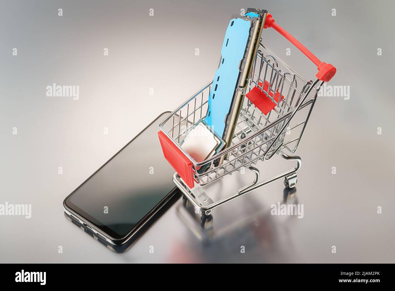 Toy shopping cart with computer components and smartphone. On a gray background with reflection. Sale and purchase of electronics and online trade the Stock Photo