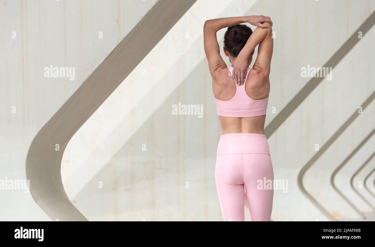 Rear view of a sporty woman doing an arm stretch exercise, warming up. Urban setting. Stock Photo