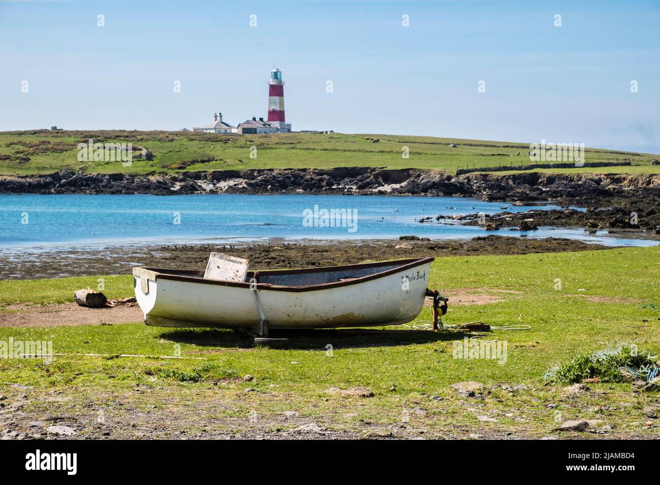Beached boat on seashore with Grey Seals in bay beyond and lighthouse on the headland. Ynys Enlli / Bardsey Island, Llyn Peninsula Gwynedd north Wales Stock Photo