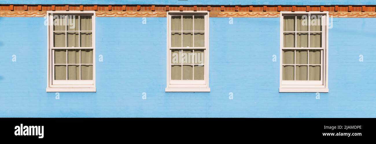 Side of an old house with blue brick wall with Victorian white wooden sash windows. UK Stock Photo