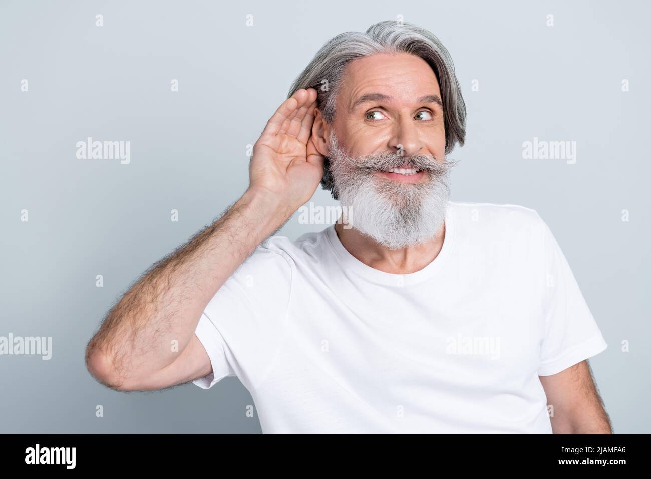 Photo of funny curious man pensioner dressed white t-shirt hearing secrets looking empty space smiling isolated grey color background. Stock Photo
