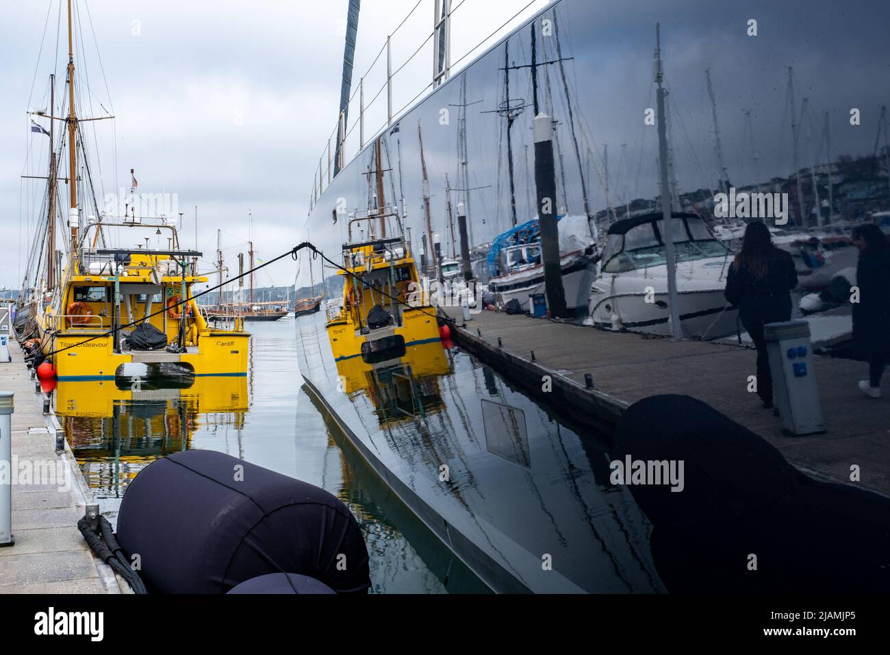 Reflections of working boats and marina, in the incredibly polished hull of a multi million pound super yacht moored in Falmouth. Mirror of the world Stock Photo