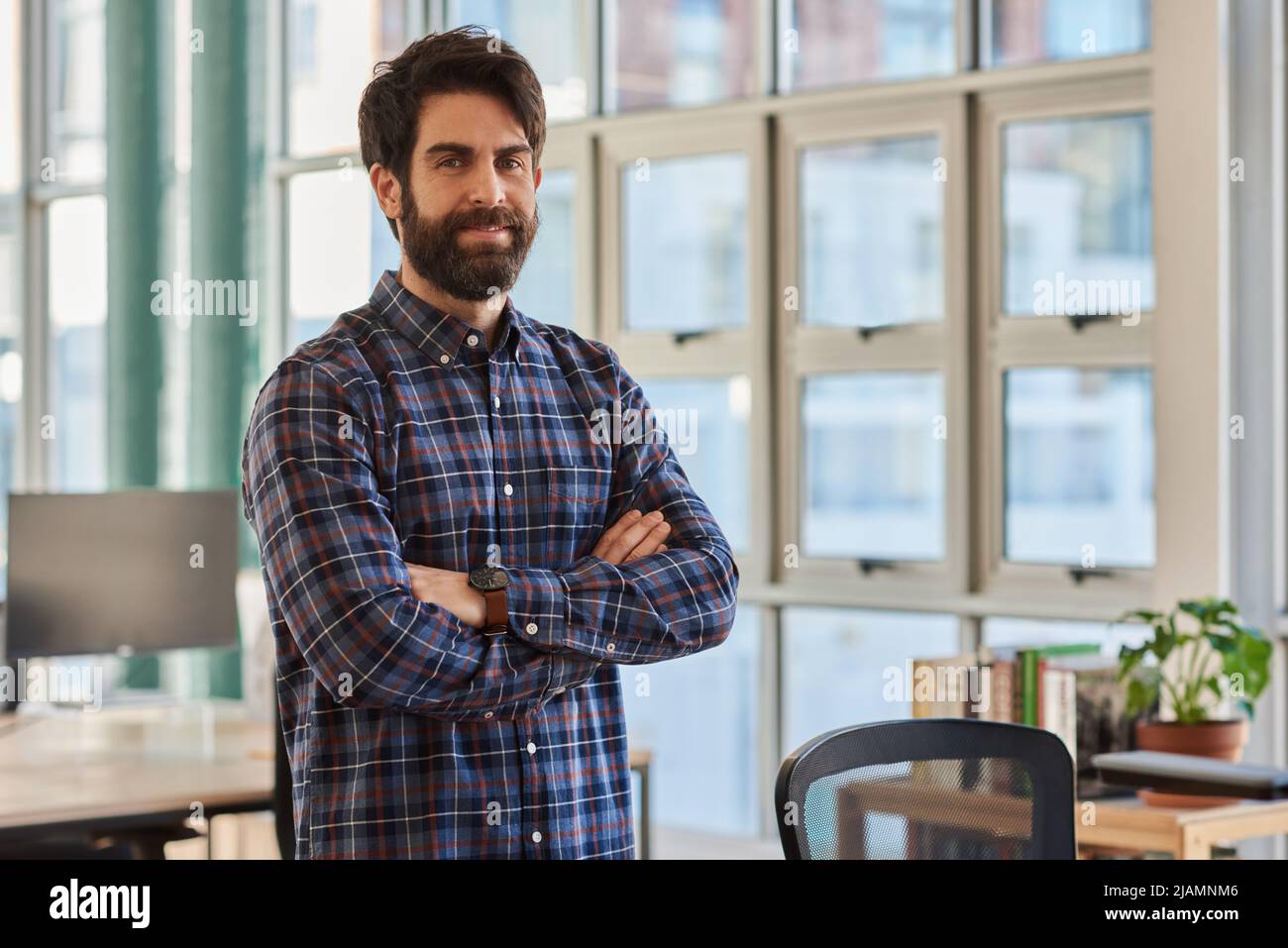 Businessman smiling while standing with his arms crossed in an office ...