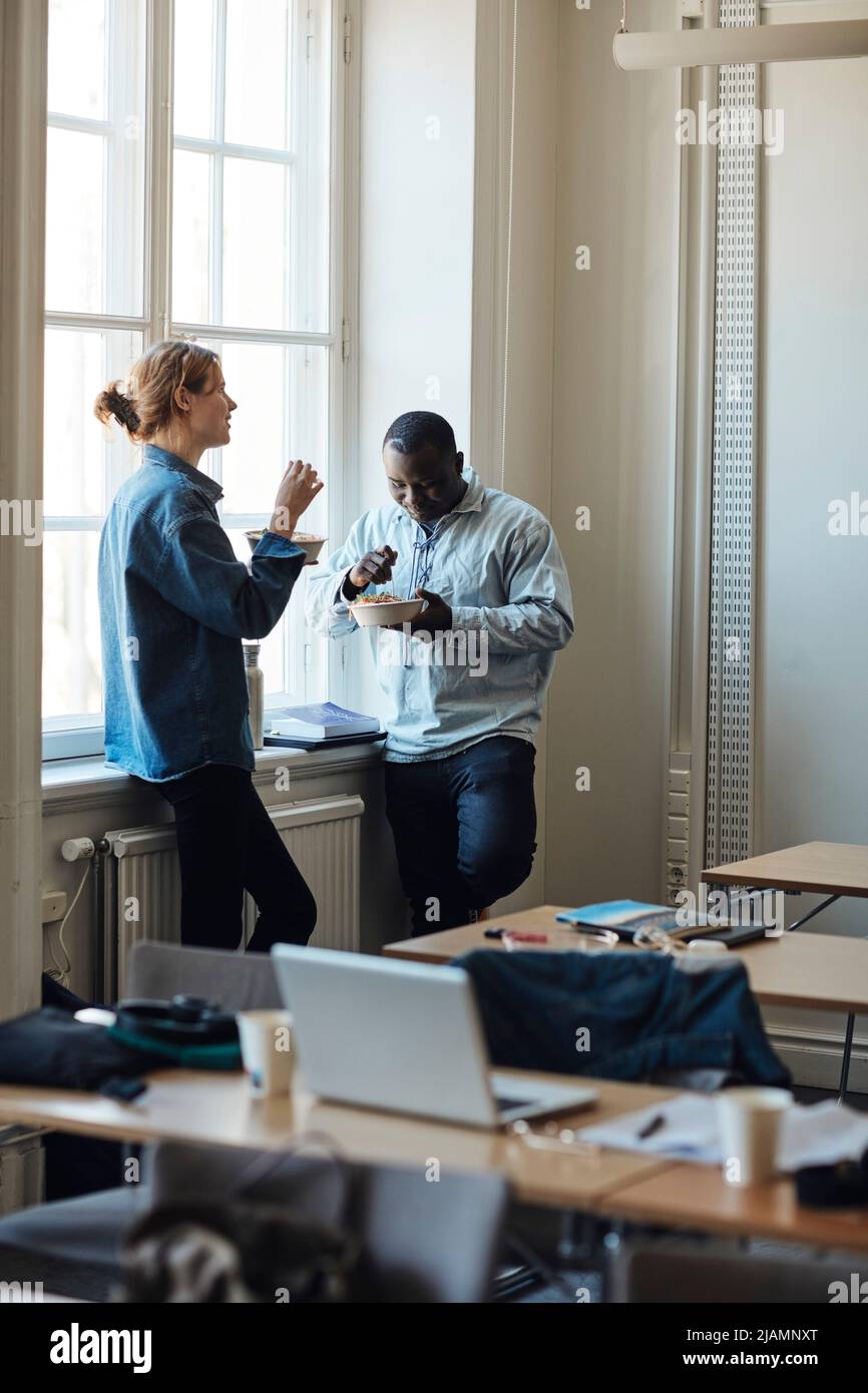 Friends eating food by window during lunch break at school Stock Photo