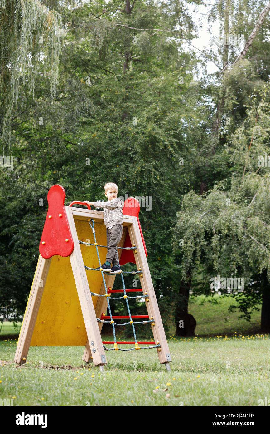 Child climb on rope net in city park. A brave child climbs up to the top. Stock Photo