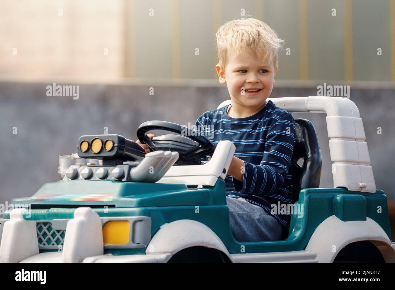 Smiling little boy driving big toy car. Child enjoying warm summer day. Copy space. Stock Photo