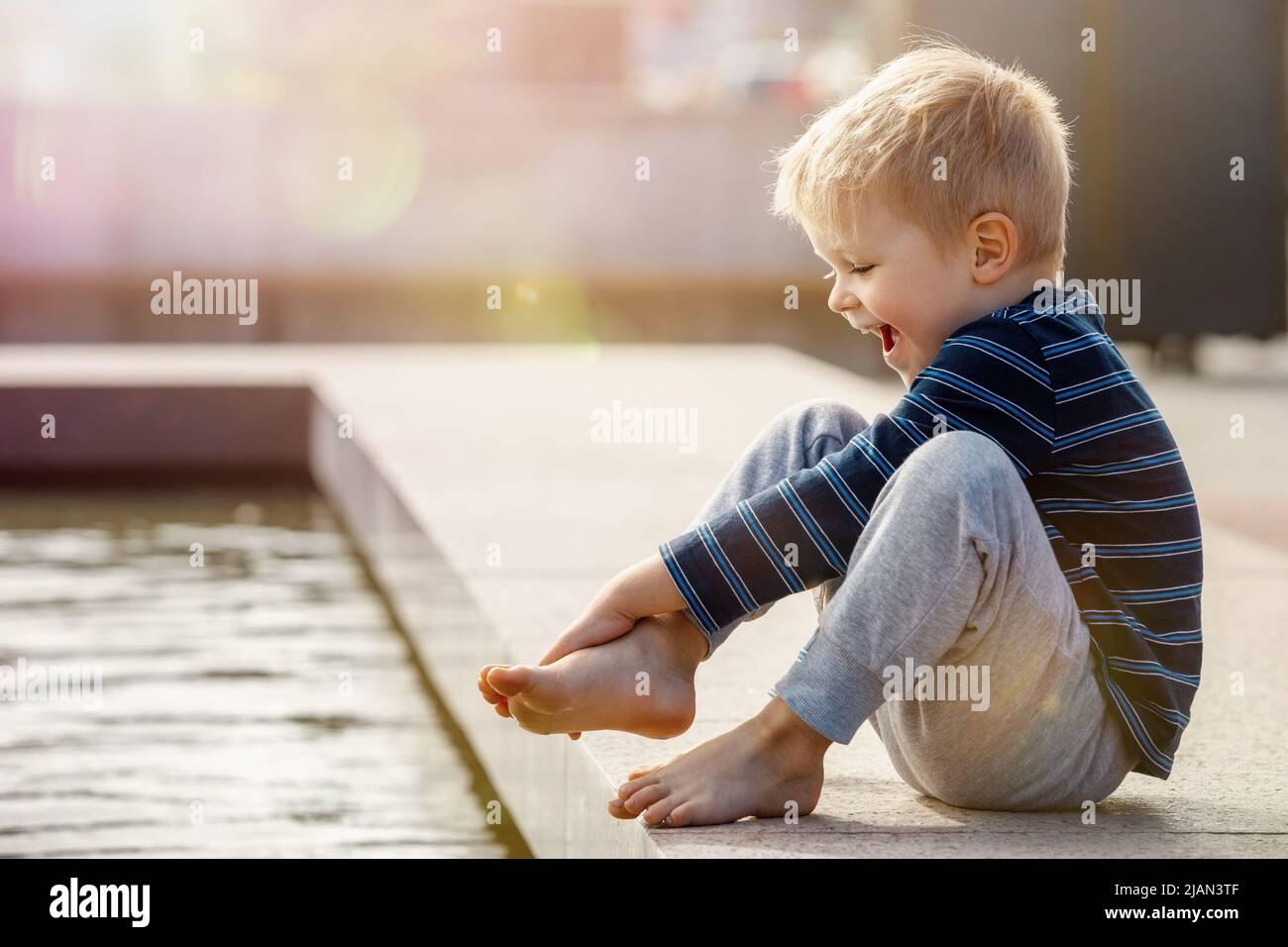 Boy having fun in water fountains. Child playing with a city fountain on hot summer day. Happy kid having fun in fountain. Summer weather. The child i Stock Photo