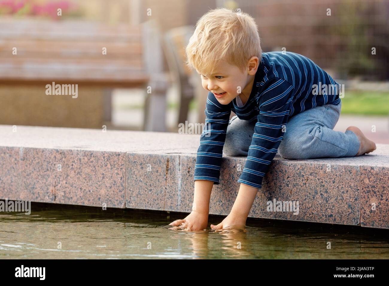 Portrait of adorable 3 years old toddler boy touching water in fountain at park. Stock Photo