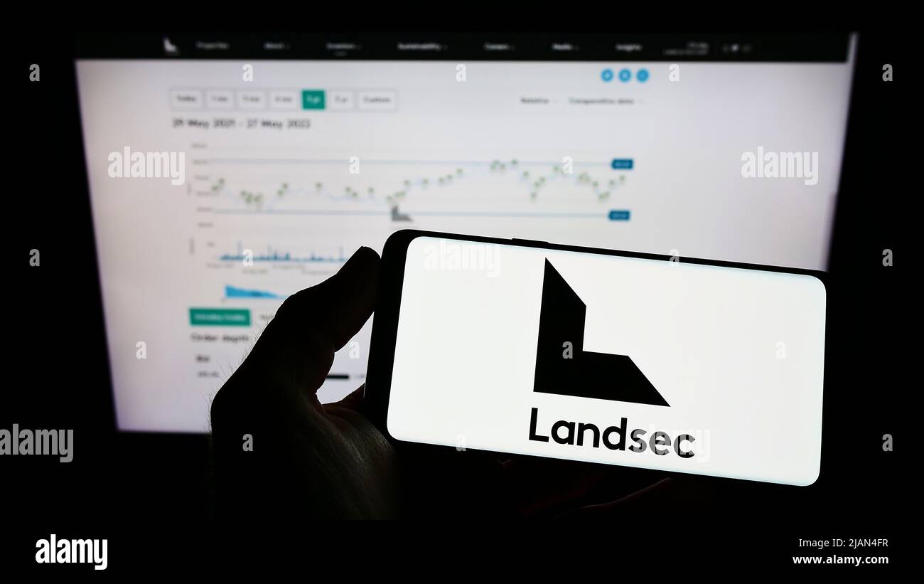 Person holding mobile phone with logo of company Land Securities Group plc (Landsec) on screen in front of web page. Focus on phone display. Stock Photo