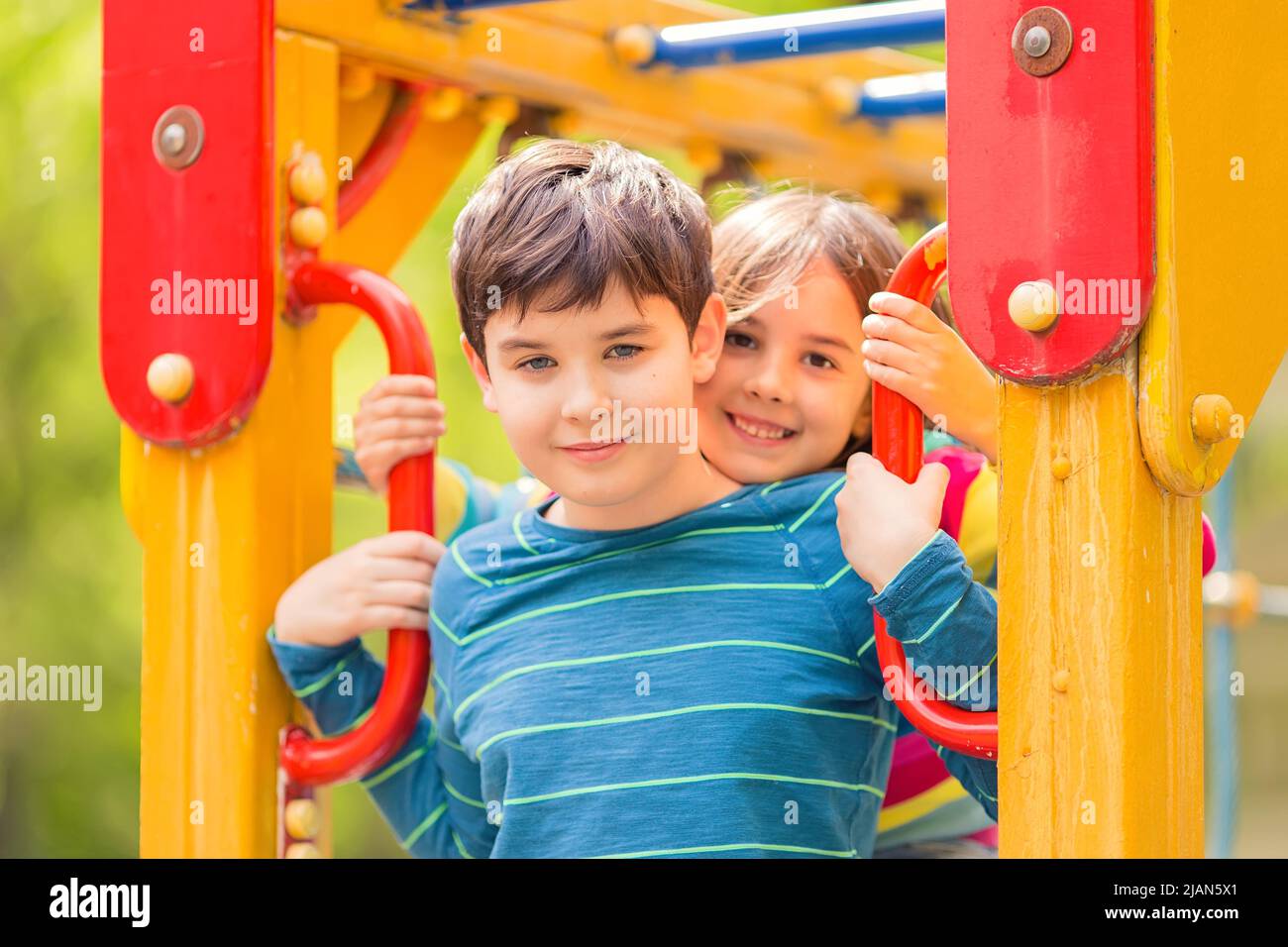 Smiling cute boy and girl, brunettes, stand among the yellow colorful playground Stock Photo