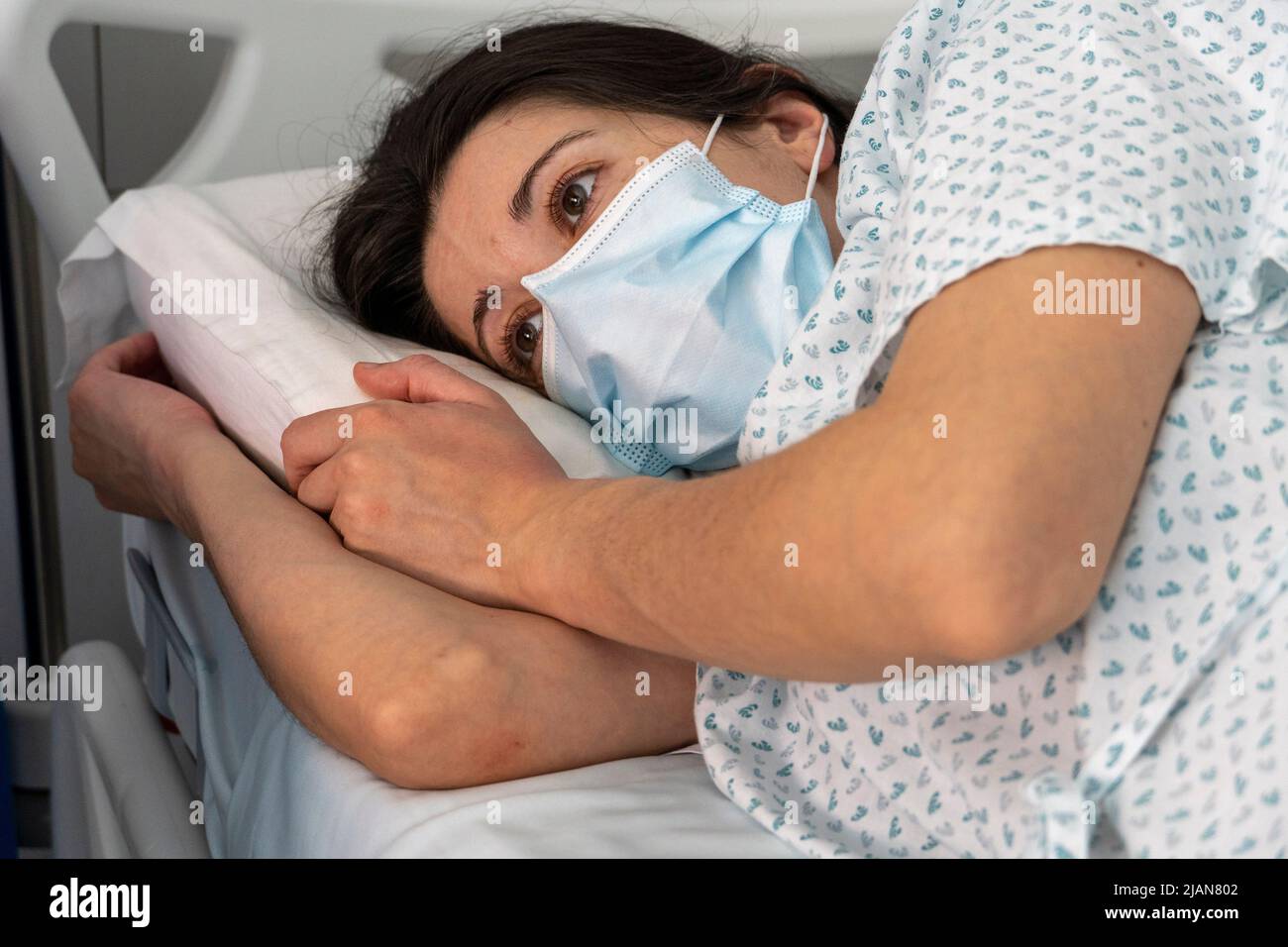 Hospitalized young woman wearing a face mask while lying in an hospital ward bed Stock Photo