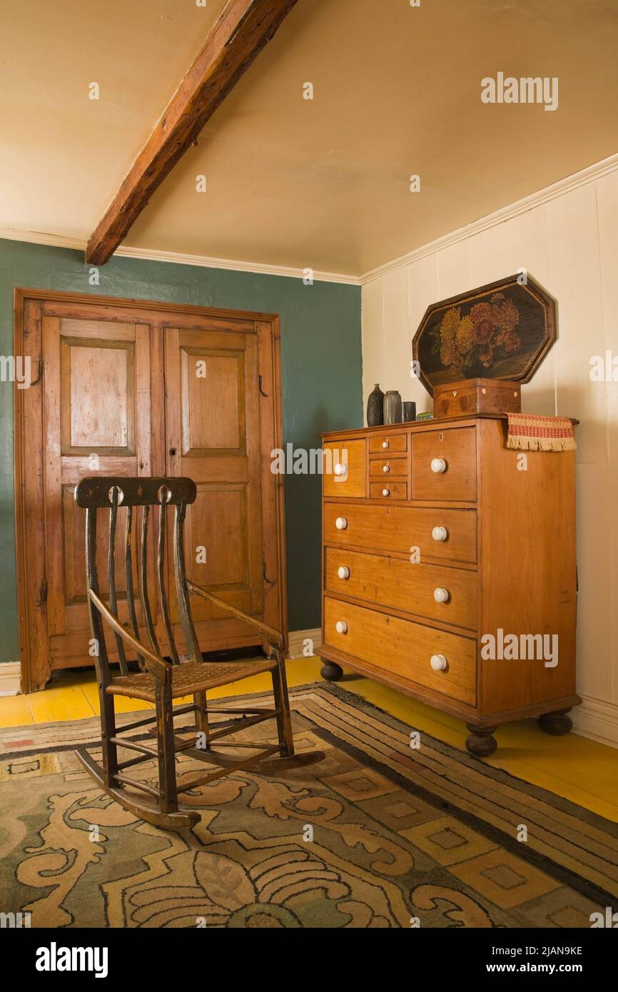 Antique rocking chair and chest of drawers in main bedroom on upstairs floor inside old circa 1810 Canadiana cottage style home. Stock Photo