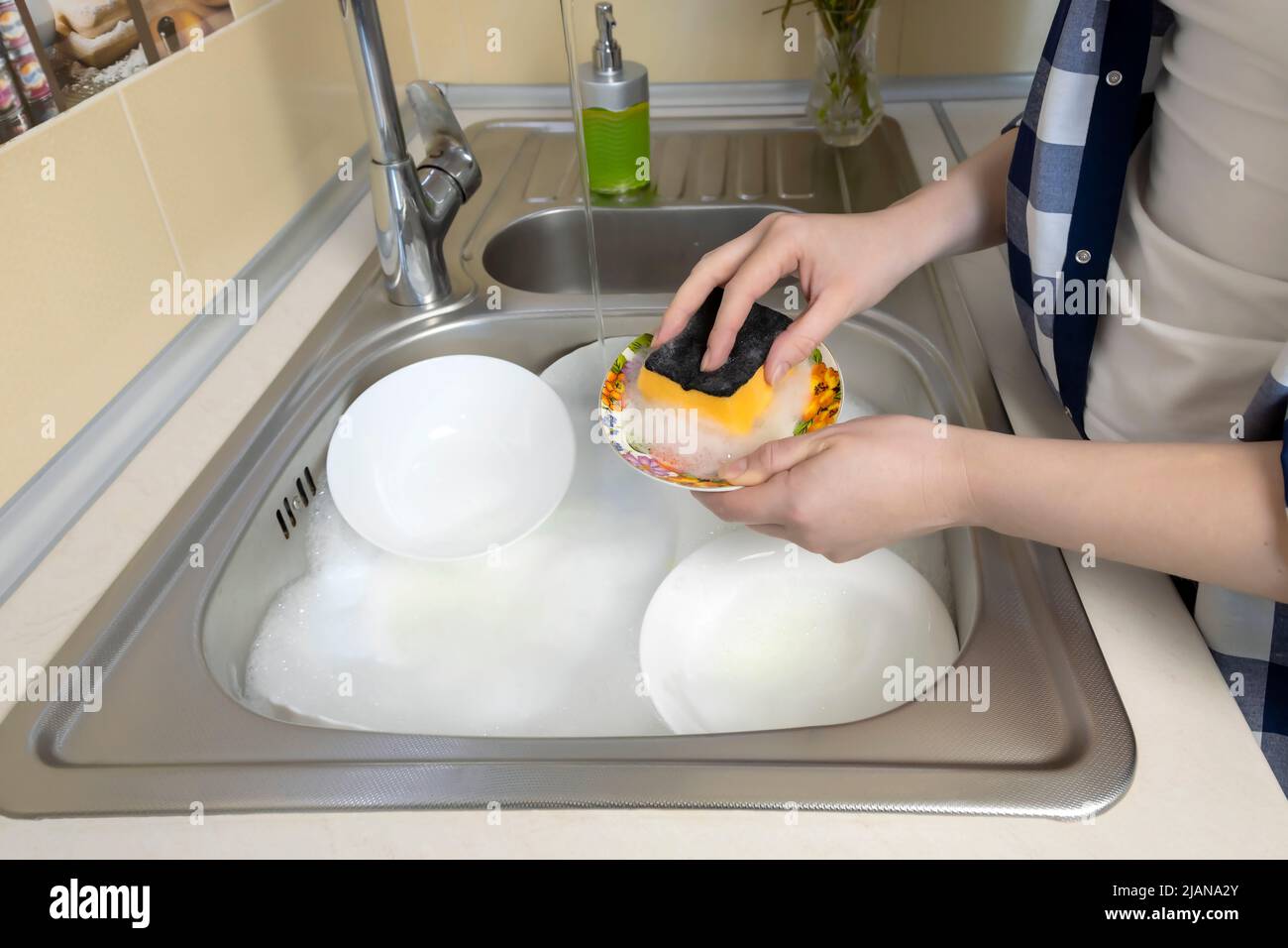 Girl washes a lot of dirty dishes in the kitchen sink. Stock Photo