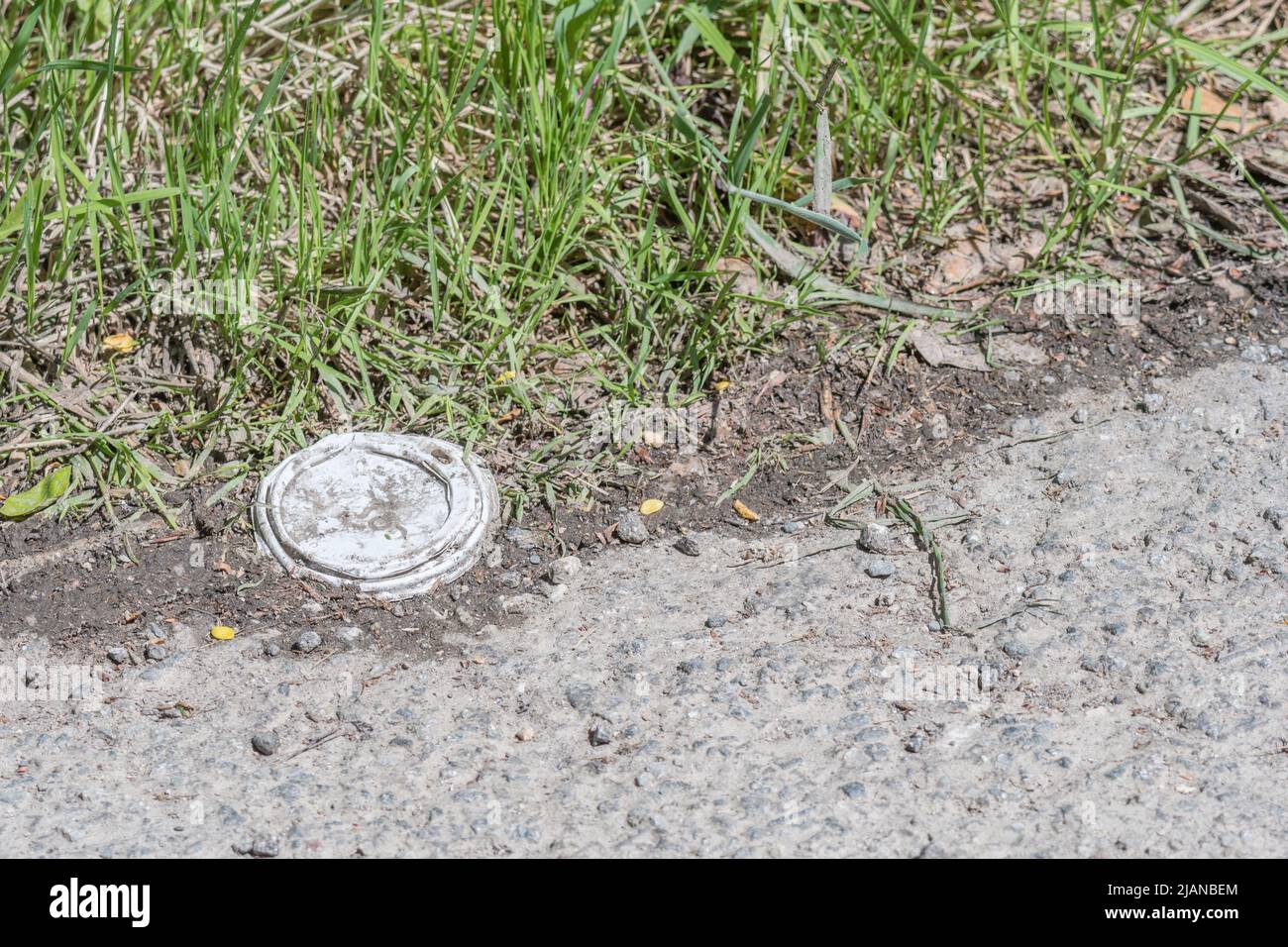 Unknown brand of takeaway coffee cup lid (assuming coffee) on country road. For war on plastic, plastic takeaway packaging, plastic litter pollution. Stock Photo