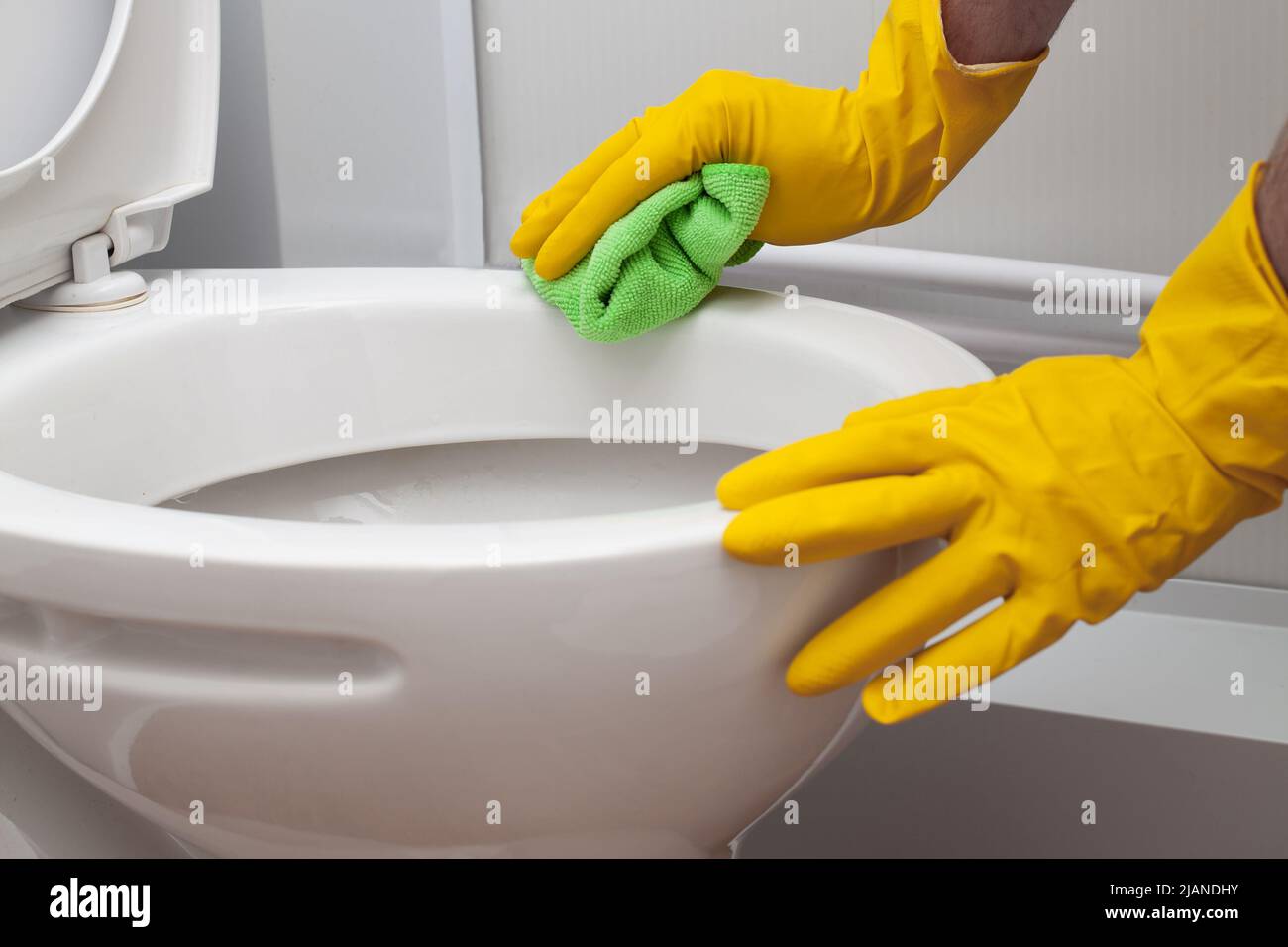 Man in yellow rubber gloves cleaning toilet with green cloth Stock