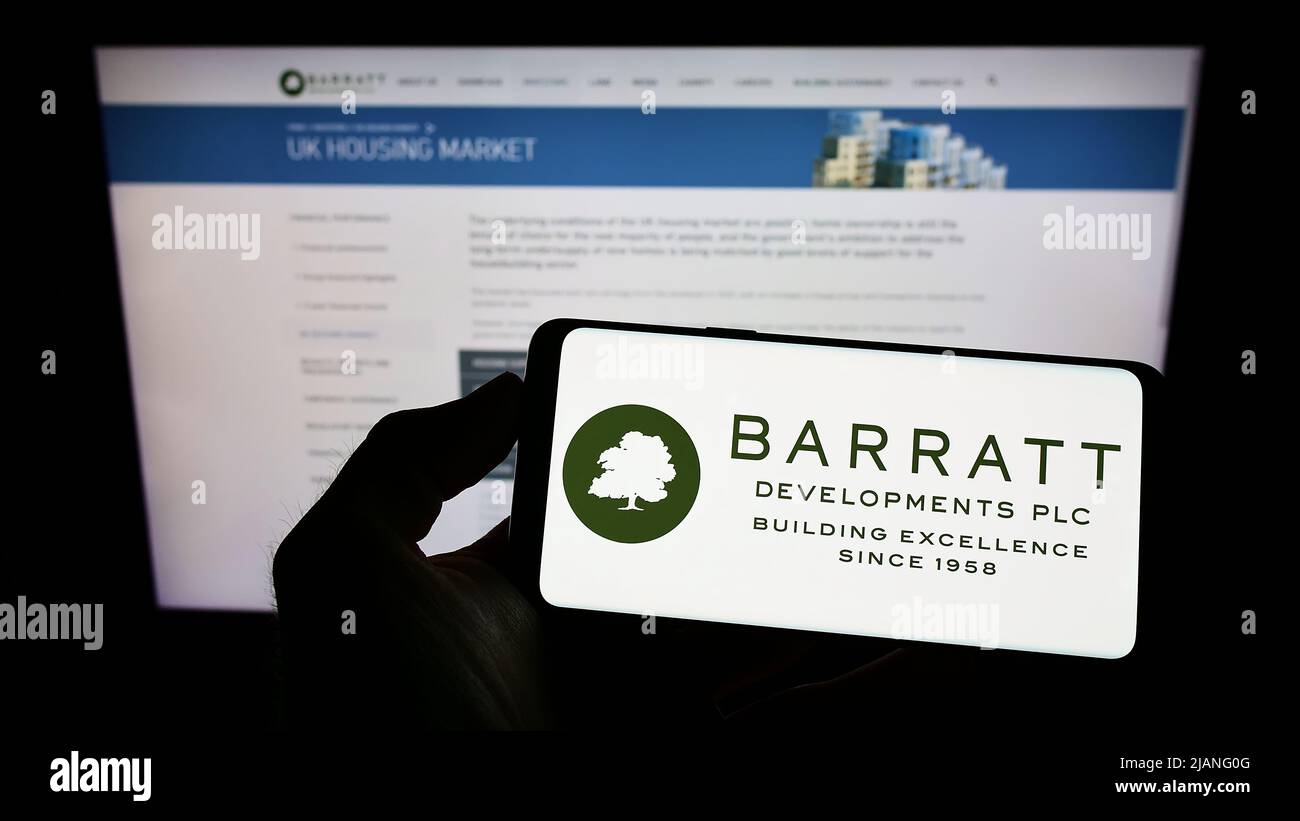 Person holding cellphone with logo of property company Barratt Developments plc on screen in front of business webpage. Focus on phone display. Stock Photo