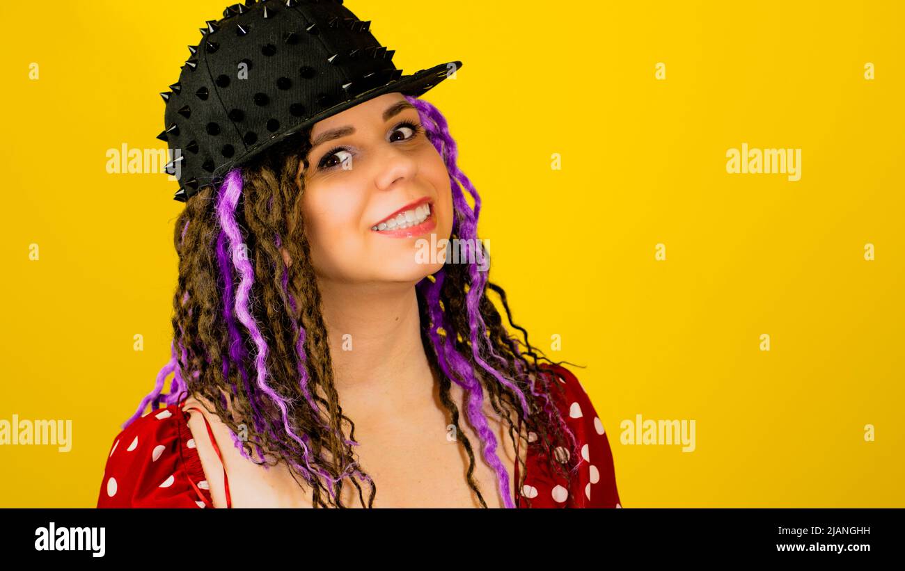 Young handsome stylish feman in black cap on yellow background. Hipster girl looking at camera with dreadlocks. Stock Photo
