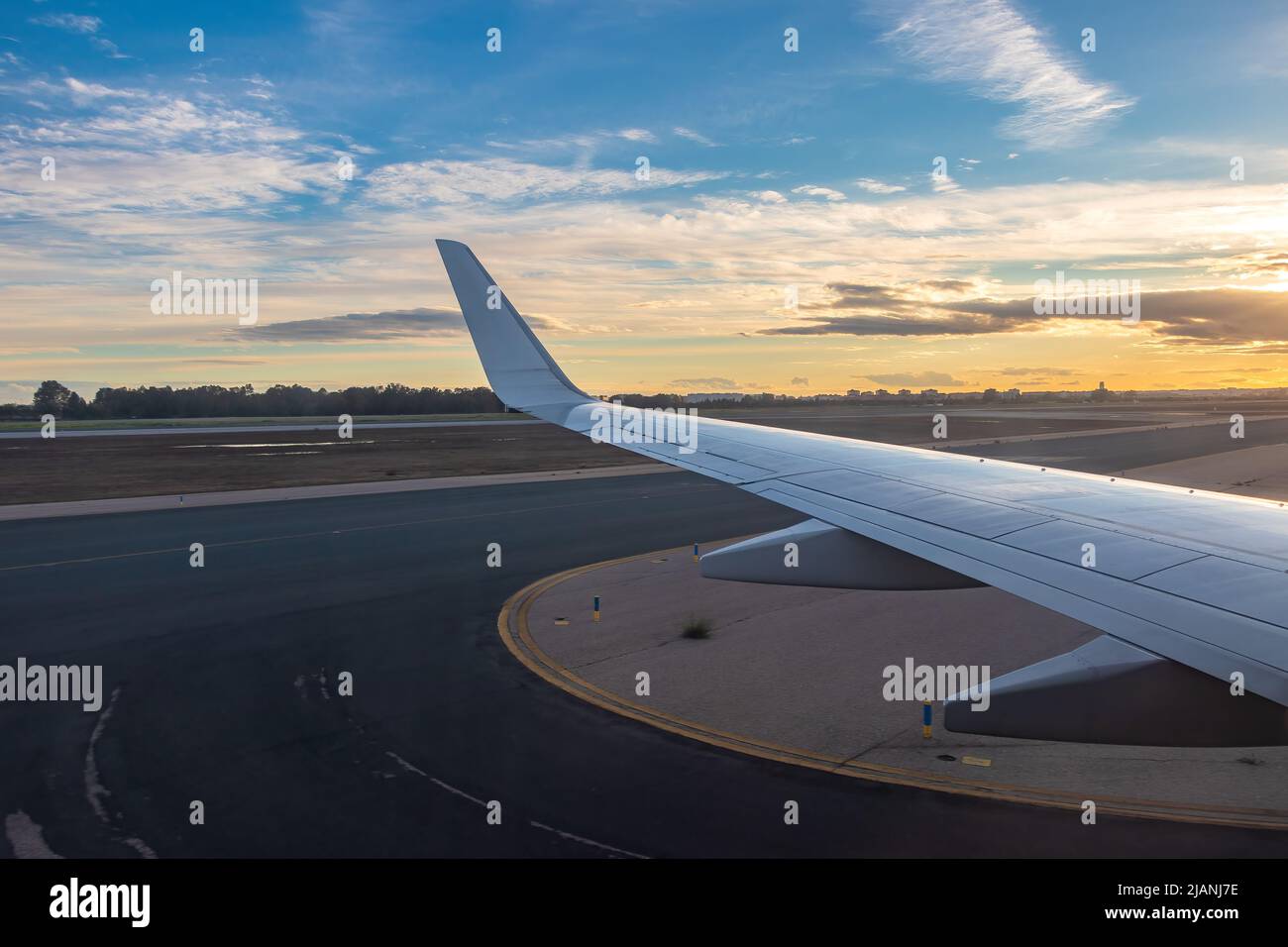 View of the plane wing from the window of passenger seat when the plane land in the airport at sunset Stock Photo