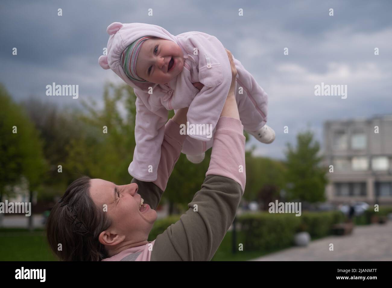 Young mother throws up baby in the sky, summer outdoors. Happy mom and ...