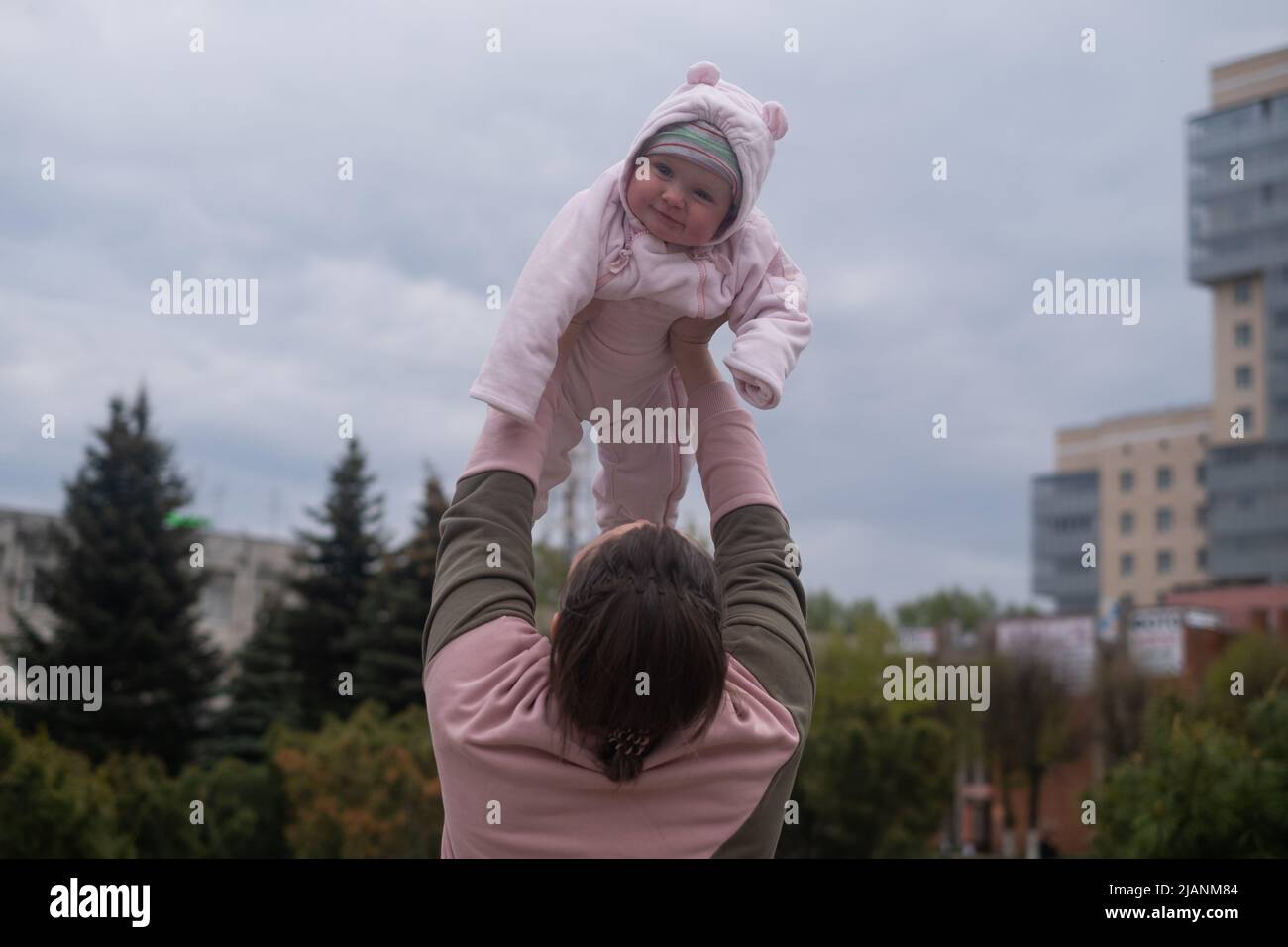 Young mother throws up baby in the sky, summer outdoors. Happy mom and ...