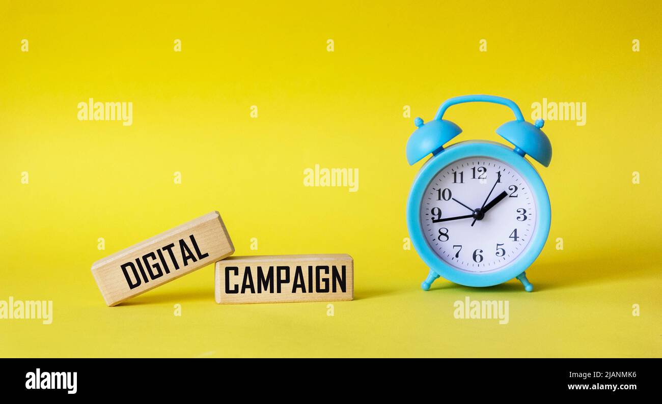The digital campaign is written on wooden blocks and a yellow background with a clock. Internet business marketing concept Stock Photo