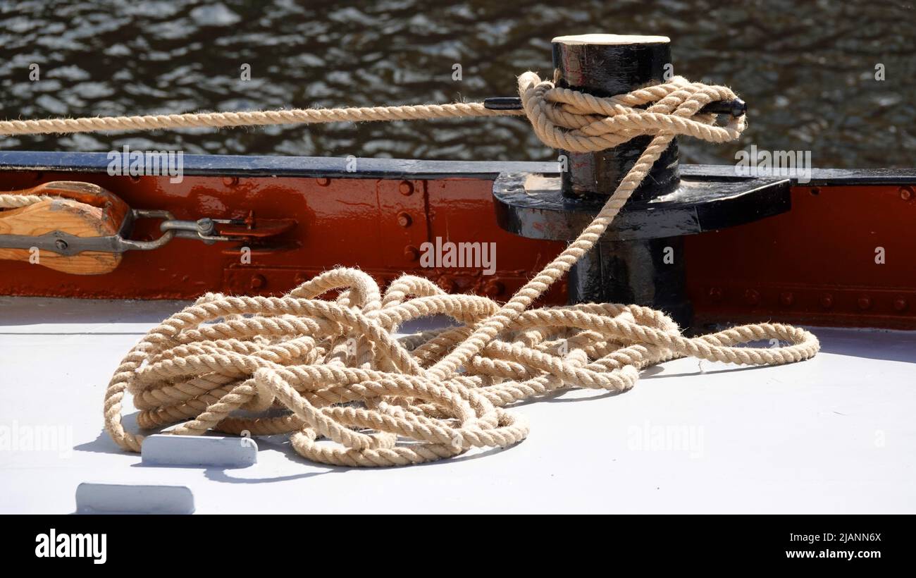 A pile of rope on the deck of a ship. It's tied to a bollard. It's  connected with a wooden pulley Stock Photo - Alamy