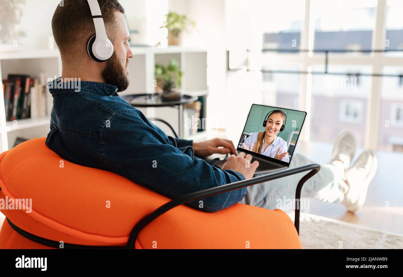 Millennial guy using wireless headset and laptop, calling business partner Stock Photo