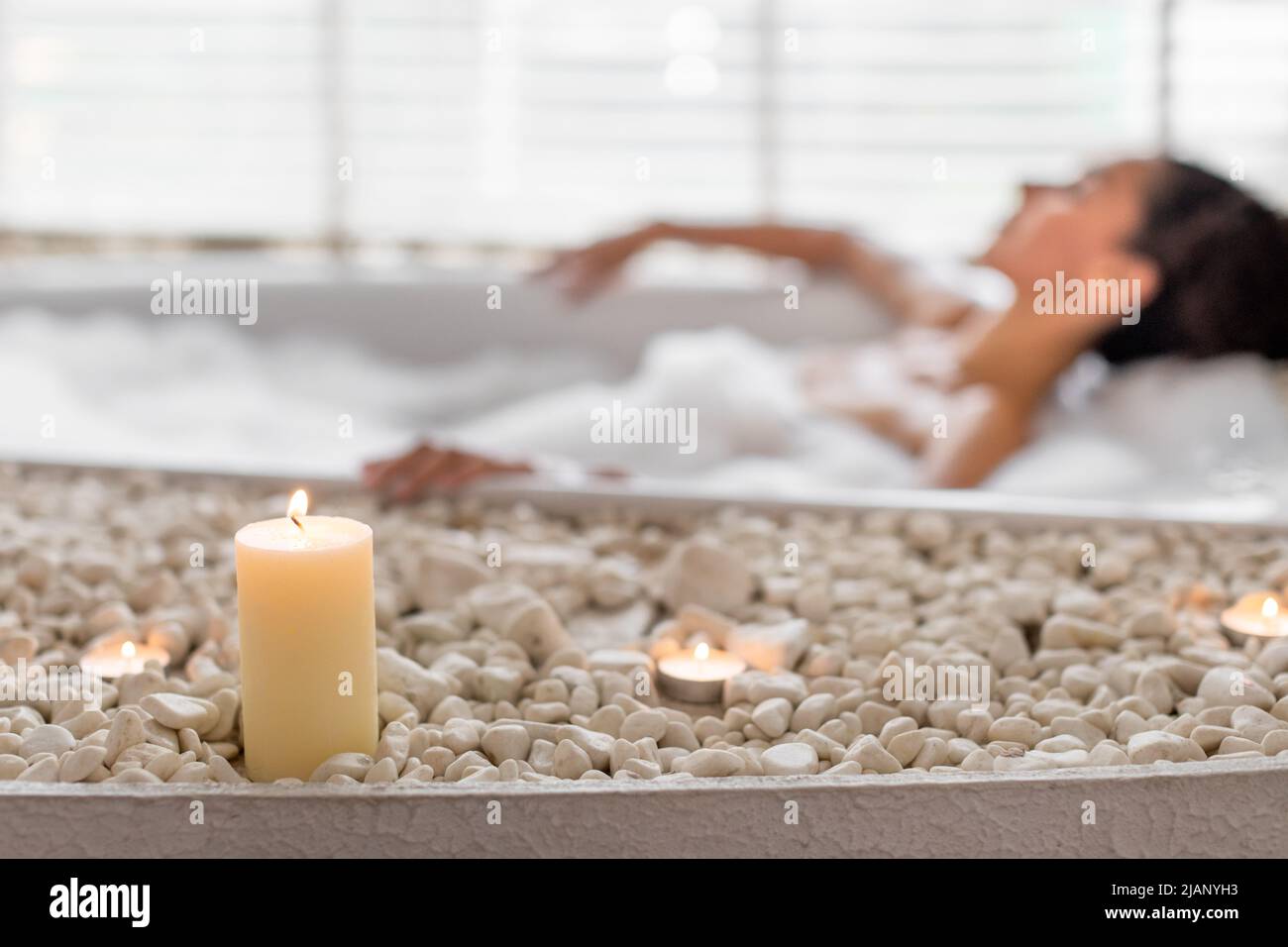 Millennial woman relaxing in bubble bath at home, selective focus on candles and stones Stock Photo