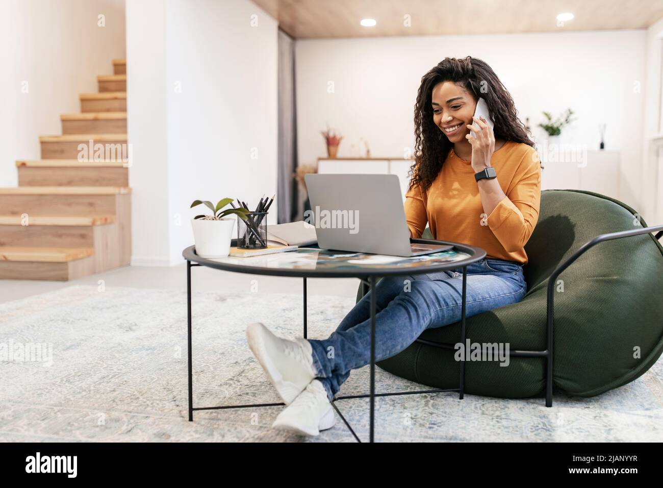 Smiling black woman working and talking on phone at home Stock Photo