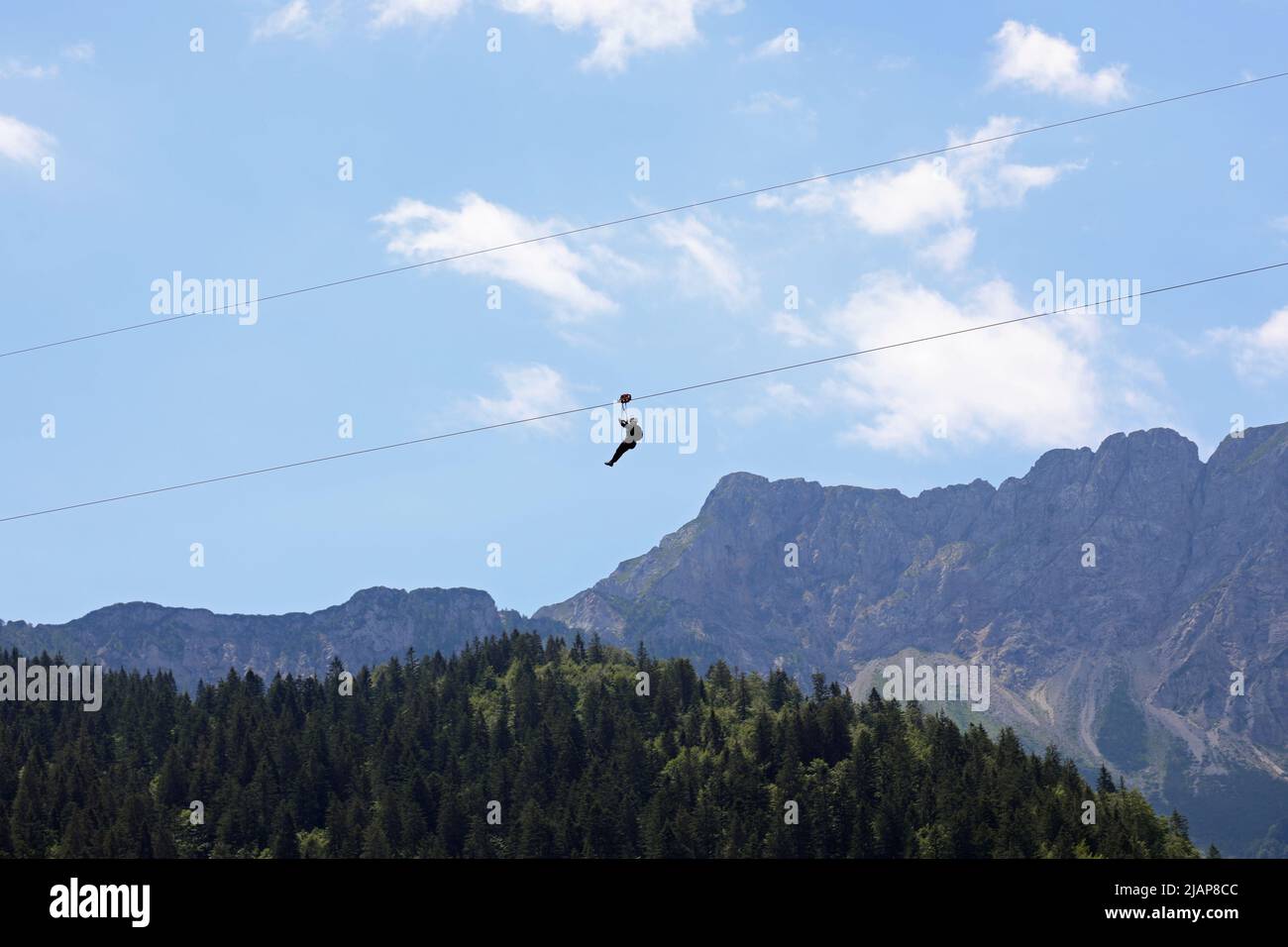 fearless person hanging from the steel cable that connects the opposite slopes of the mountain and the force of gravity that drags down and mountains Stock Photo
