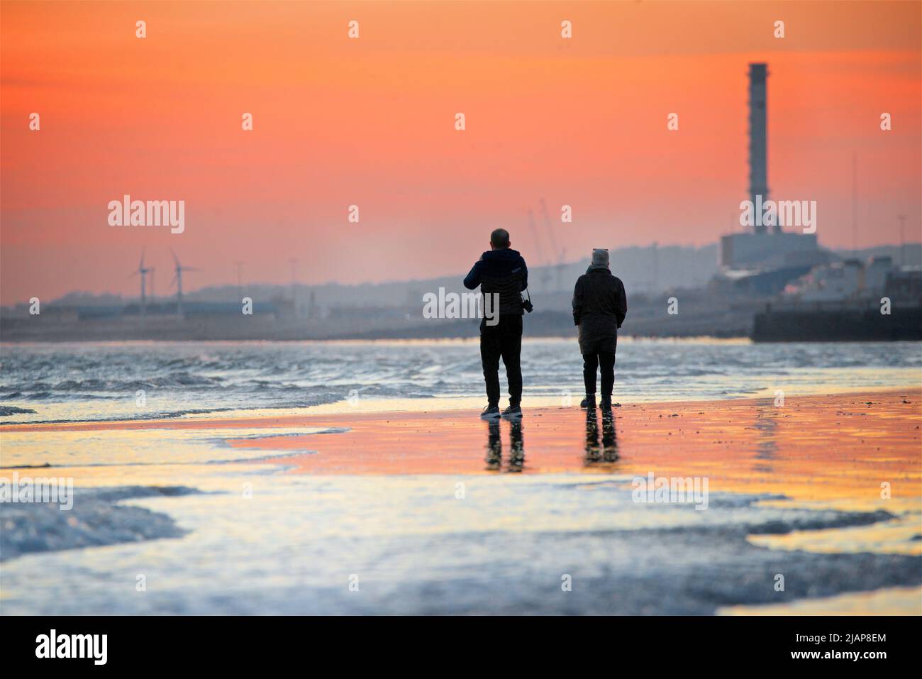 Silhouetted shapes of two people on the beach at low tide, Brighton & Hove, East Sussex, England
