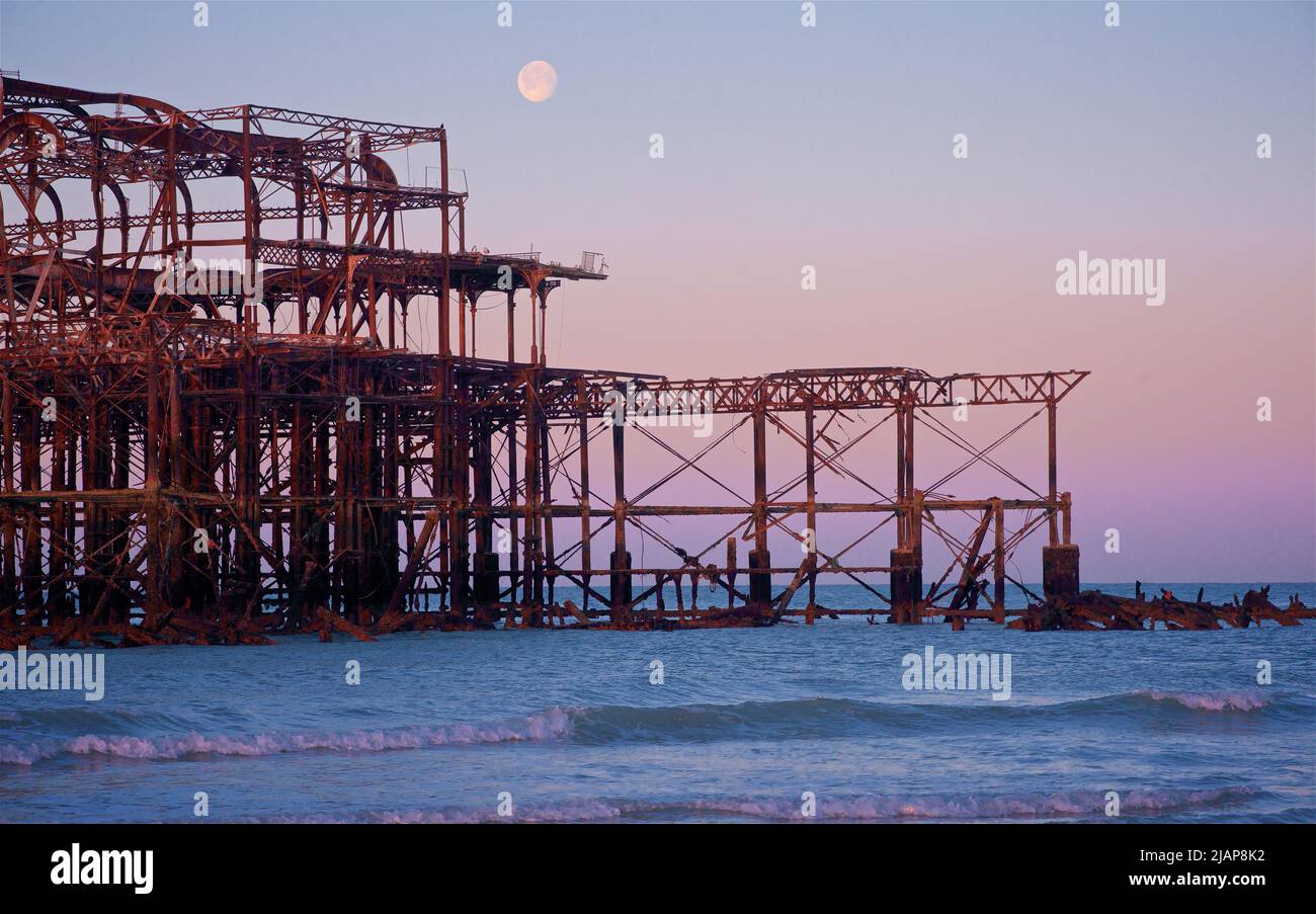 Rusting remains of the dilapidated West Pier at dawn low tide. Brighton & Hove, Sussex, England, UK. Full moon. English Channel Stock Photo