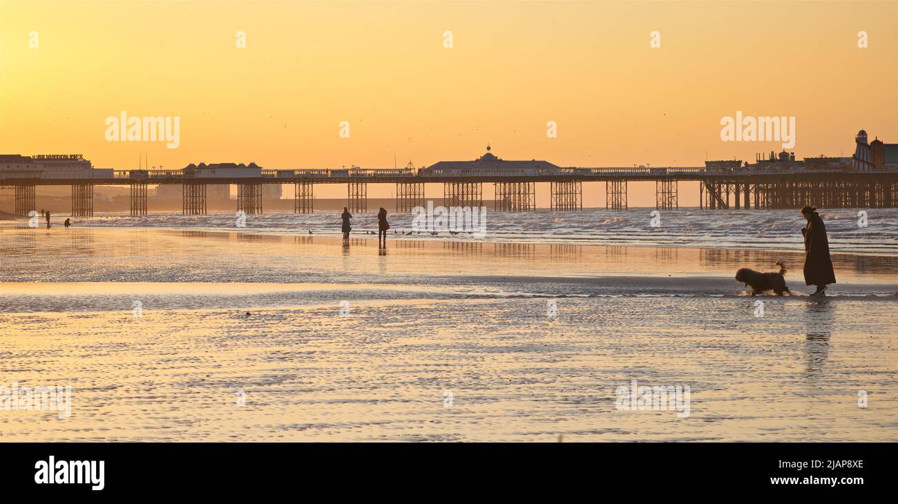 Dawn silhouettes of people on the beach at low tide, Brighton & Hove, East Sussex, England, UK