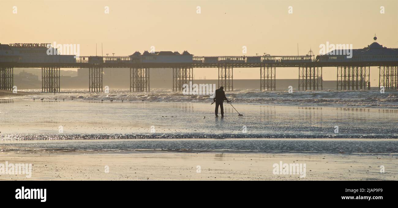 Dawn silhouette of person metal detecting on the beach at low tide