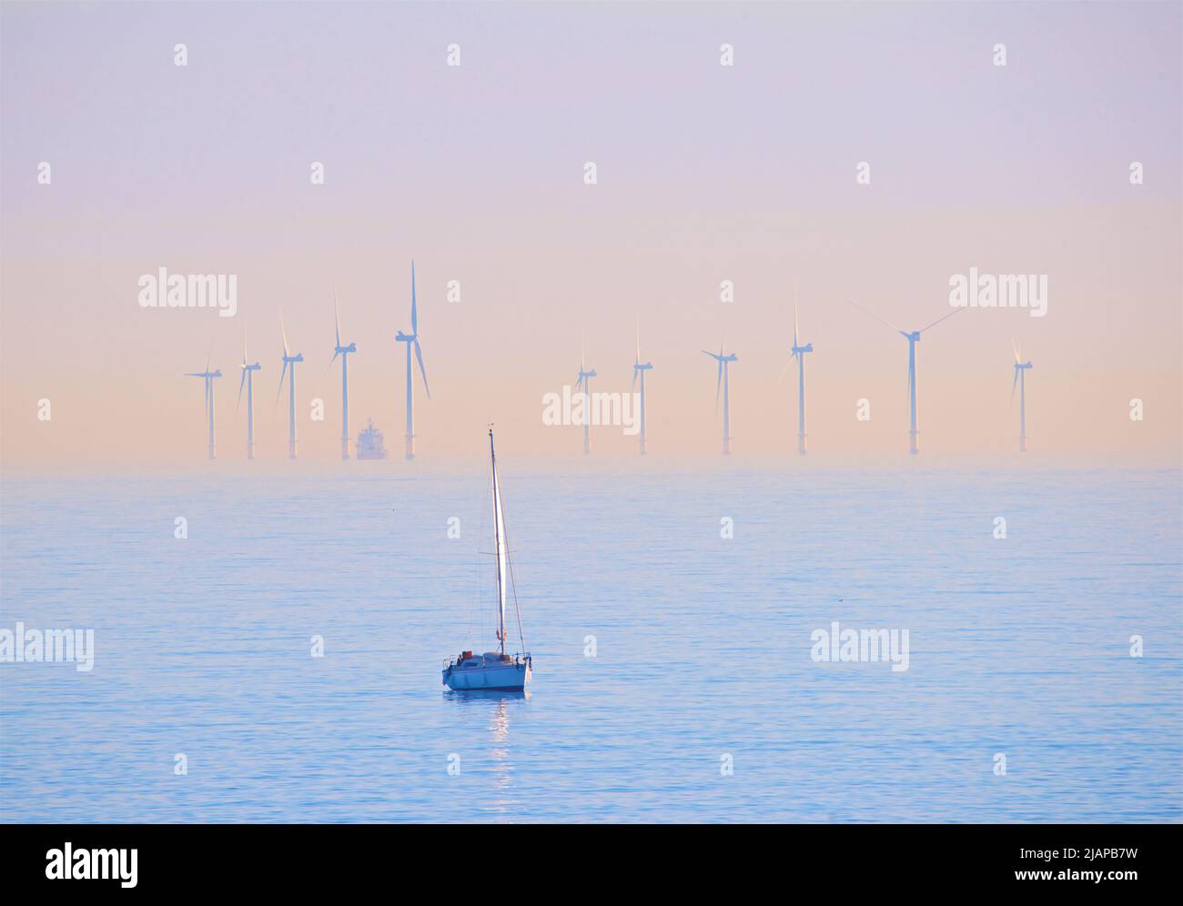 Turbines of the Rampion offshore windfarm located off the coast of Sussex, England, UK. Commissioned and produccing renewable energy in 2018, the 116 turbine windfarm cost £1.3 to build. Yacht in the foreground. Stock Photo