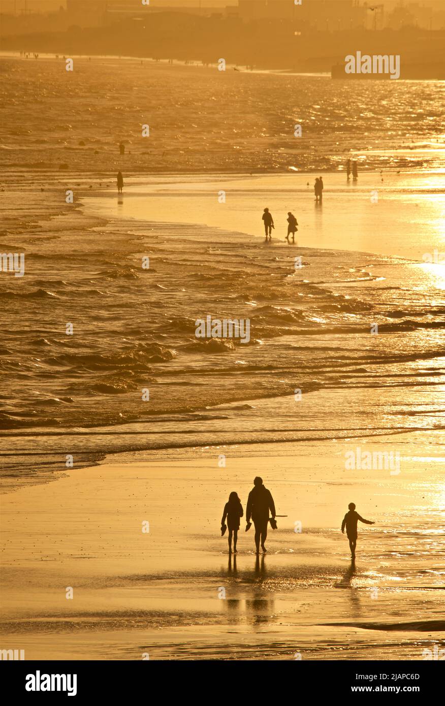 Silhouetted shapes of people walking on the exposed sand beach at low tide, Brighton & Hove, East Sussex, England, UK. Stock Photo