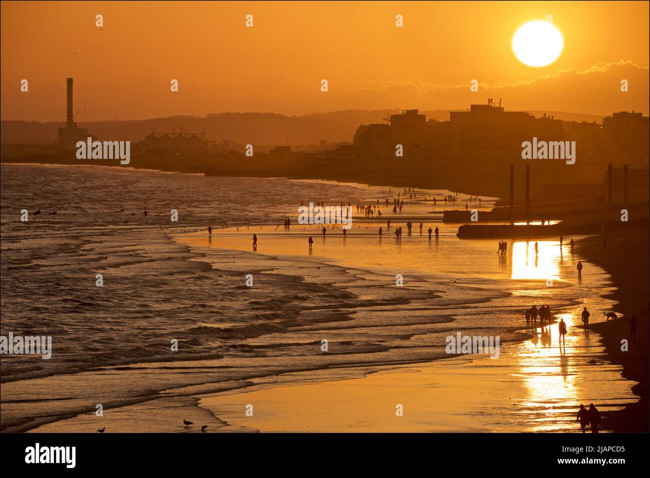 Silhouetted shapes of people on the beach at low tide, Brighton & Hove, East Sussex, England, UK