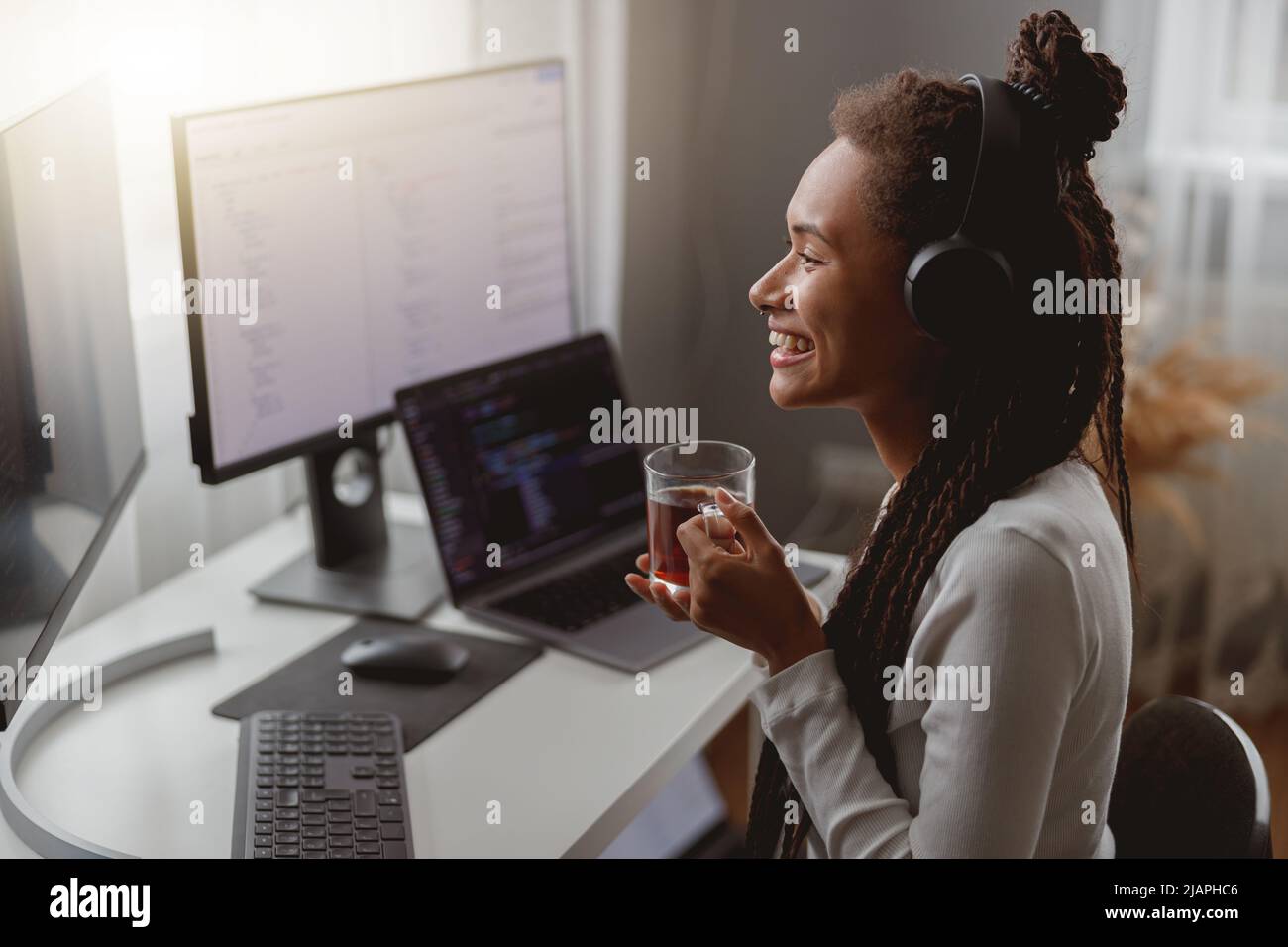 Side view of cheerful young female wearing headphones and programming on computer Stock Photo