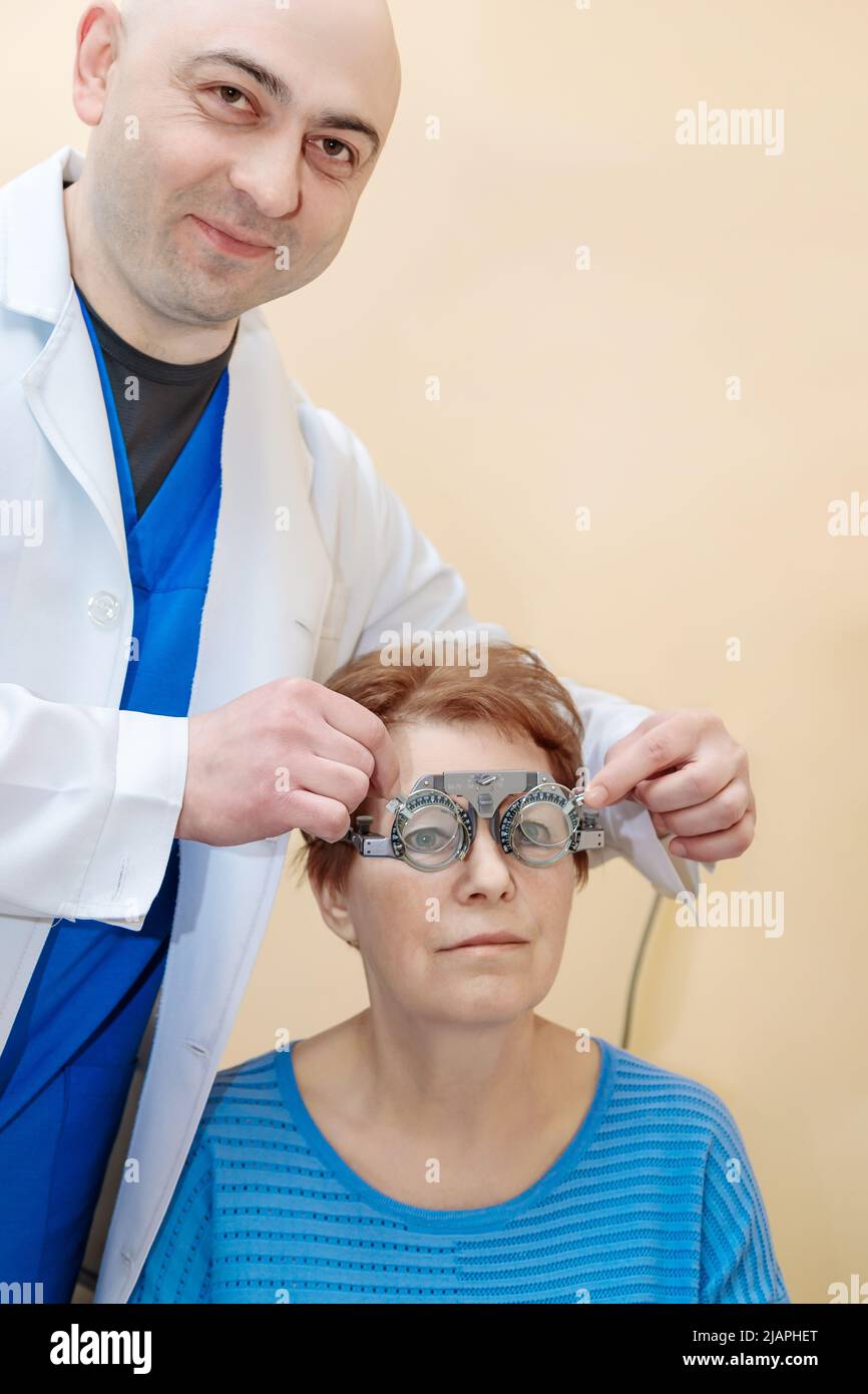 A male optometrist checks the eyesight of an adult woman with a trial frame. Stock Photo