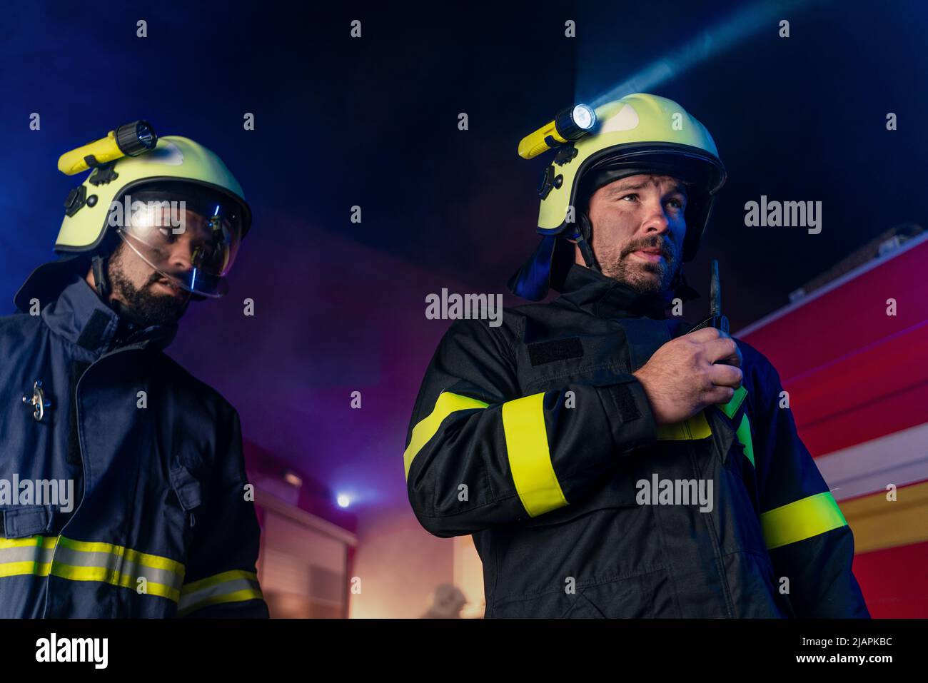 Firefighter talking to walkie talkie with fire truck in background at night. Stock Photo