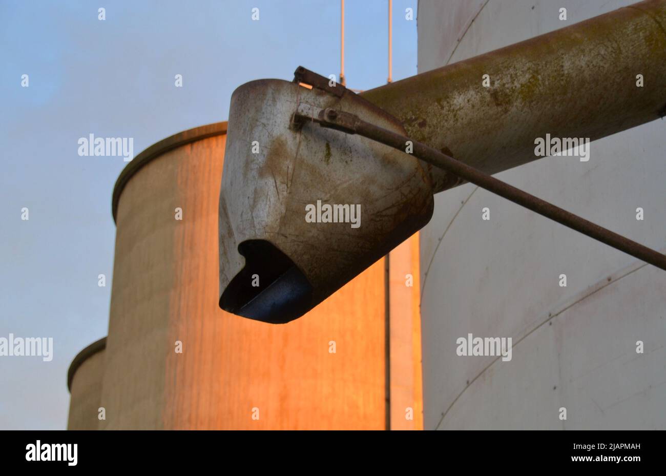 Close up of a metal or steel grain hopper in the early morning light with silos in the background in regional Australia Stock Photo